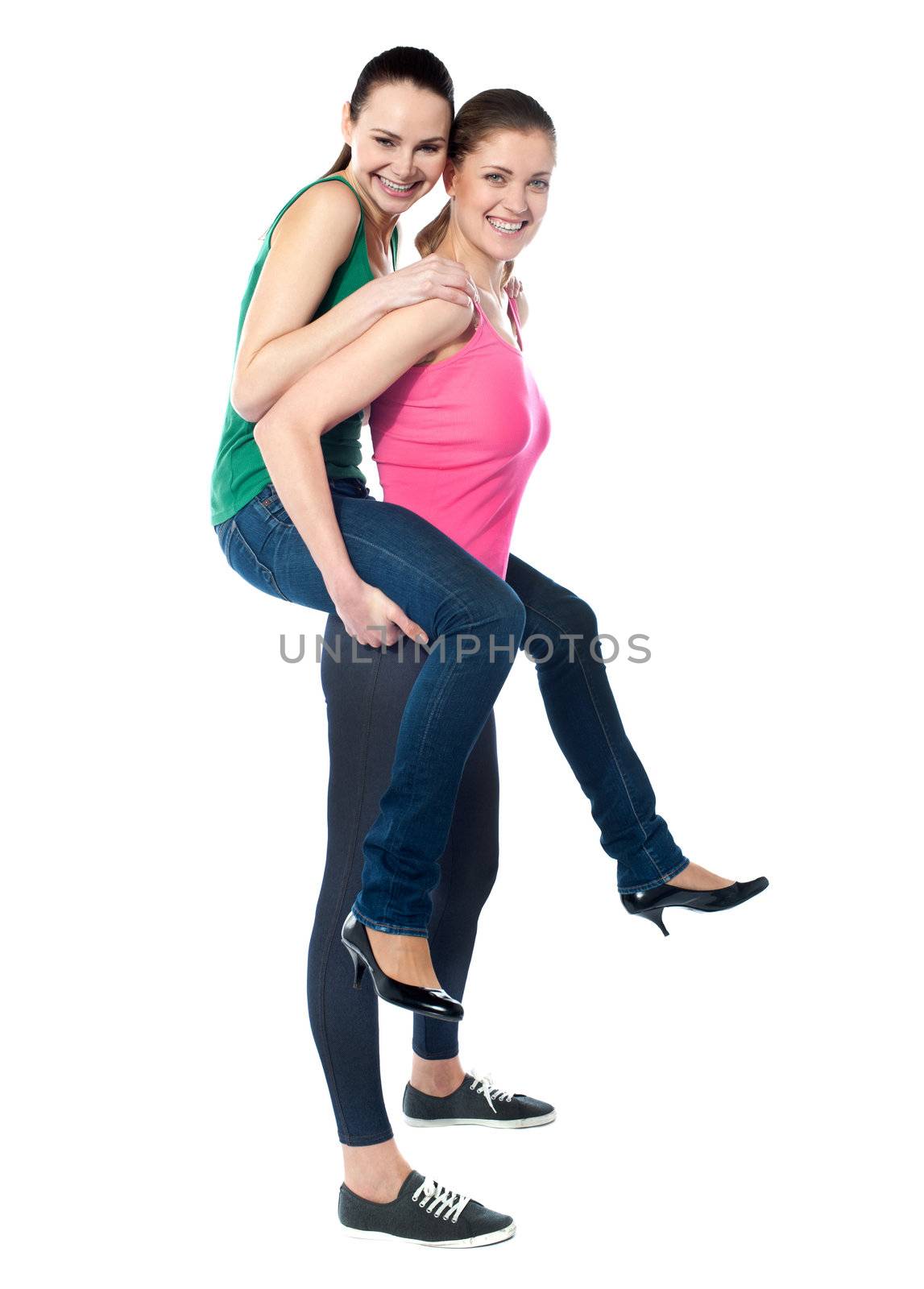 Teenage girl piggybacks her friend, studio shot