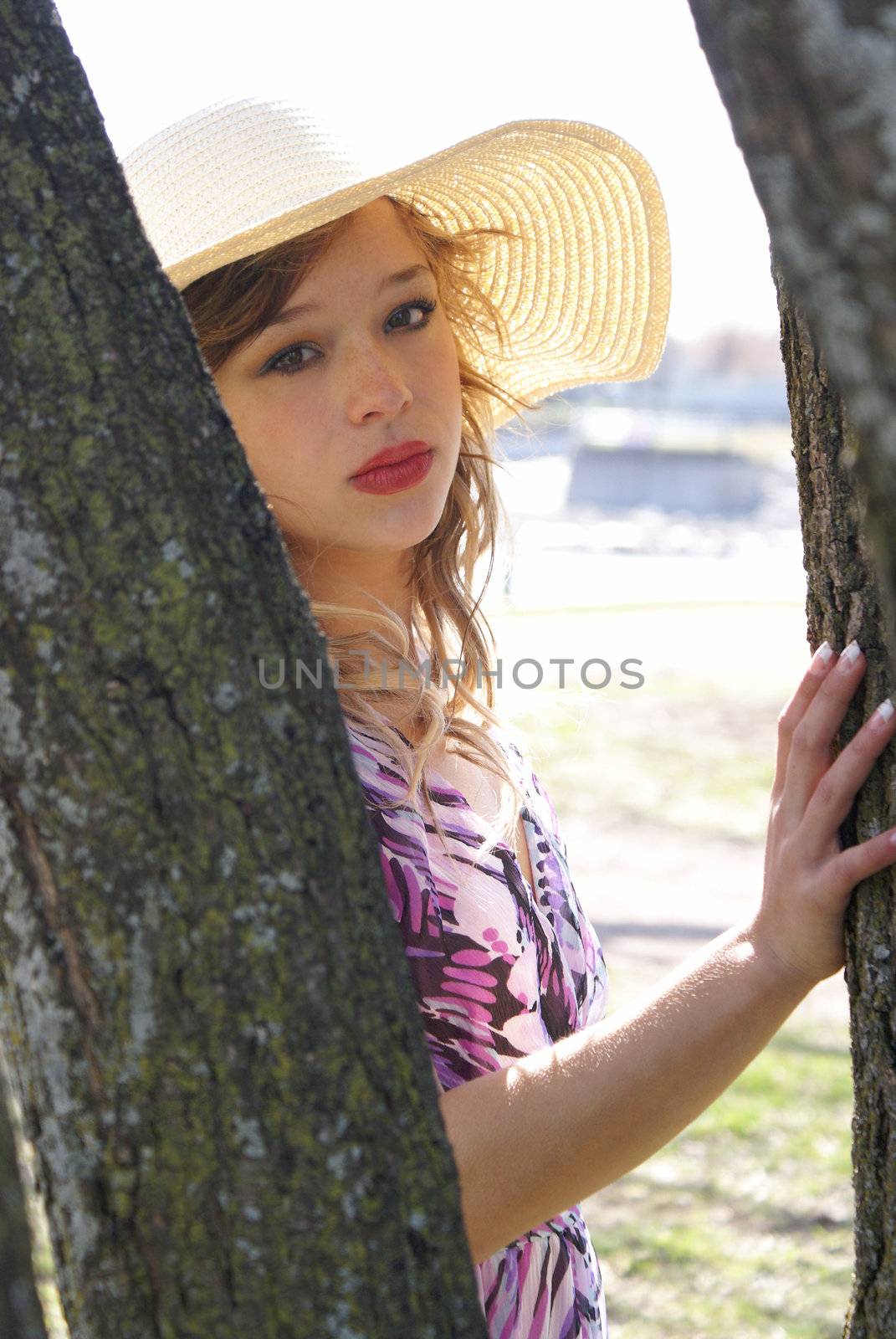 A young woman stands in the sunshine next to a tree.