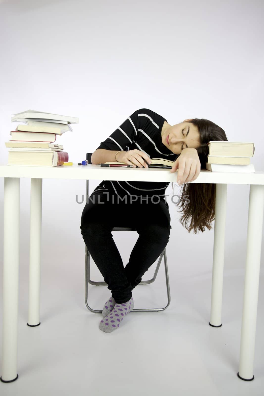 Girl sleeping while studying sitting in front of a desk full of books
