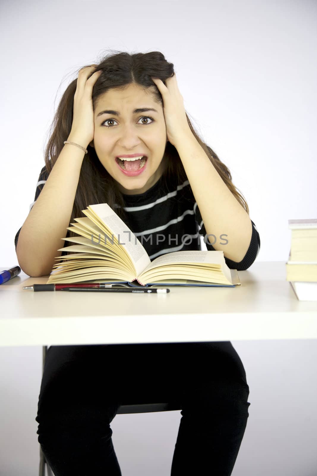 Girl studying book on a desk shouts desperate with hands in her long hair