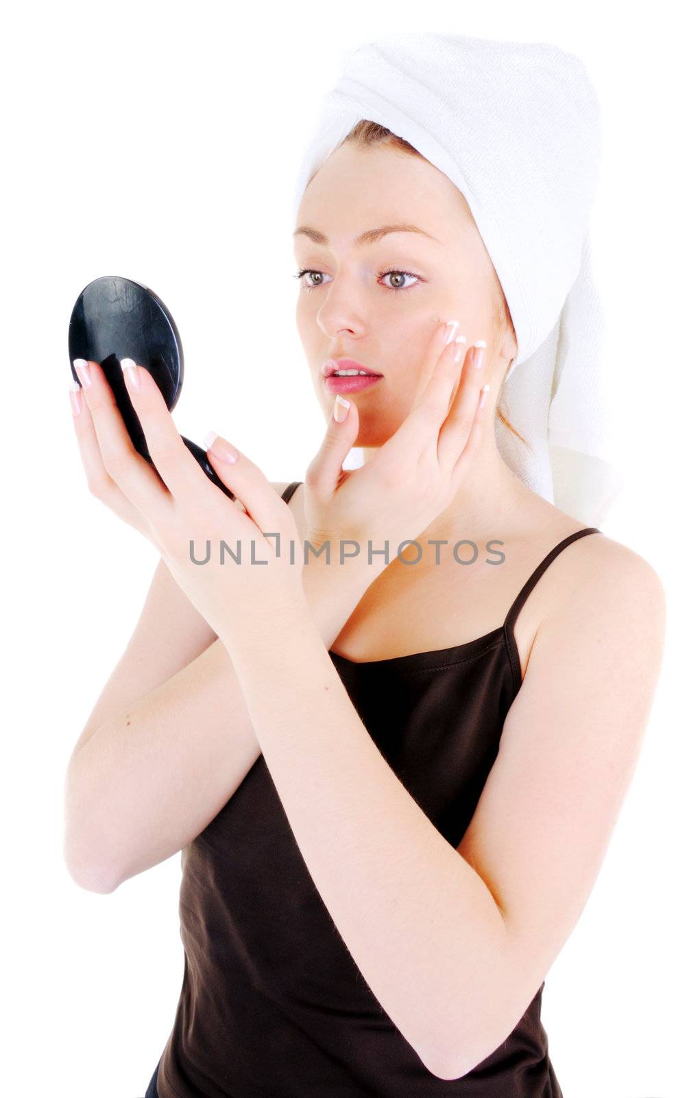 Young woman with white tower and nice manicure is appling cream on her face and looking in the looking glass, on white background