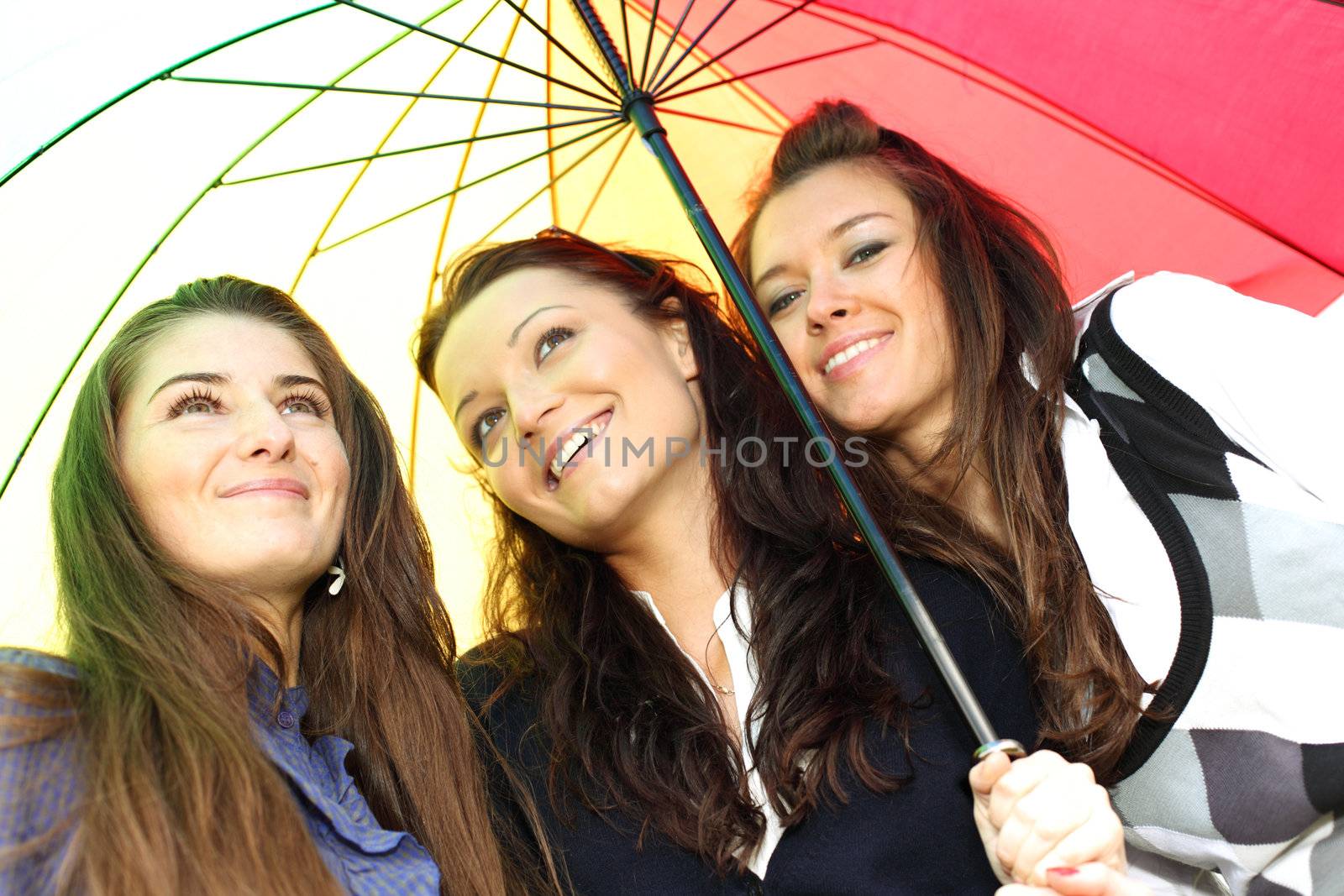 happy smiling girlfriends stay under colourful umbrella  