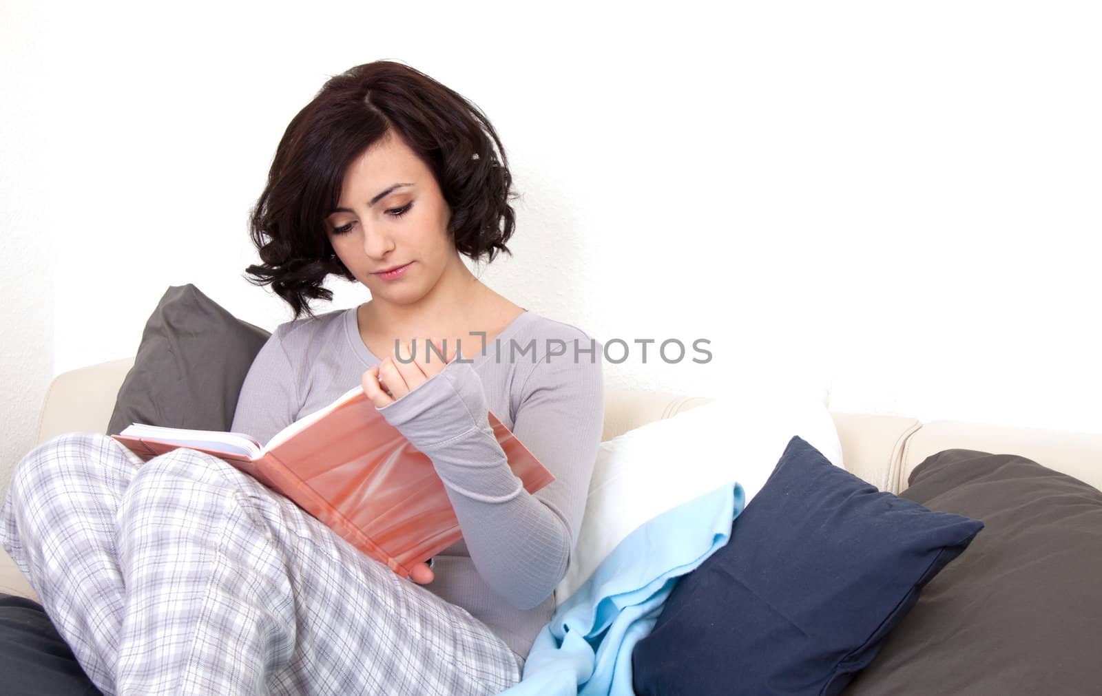 beautiful woman is sitting on the sofa an reading a book 