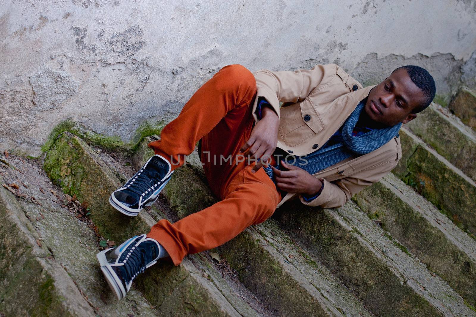 black man sitting on stairs outdoor with jacket and scarf