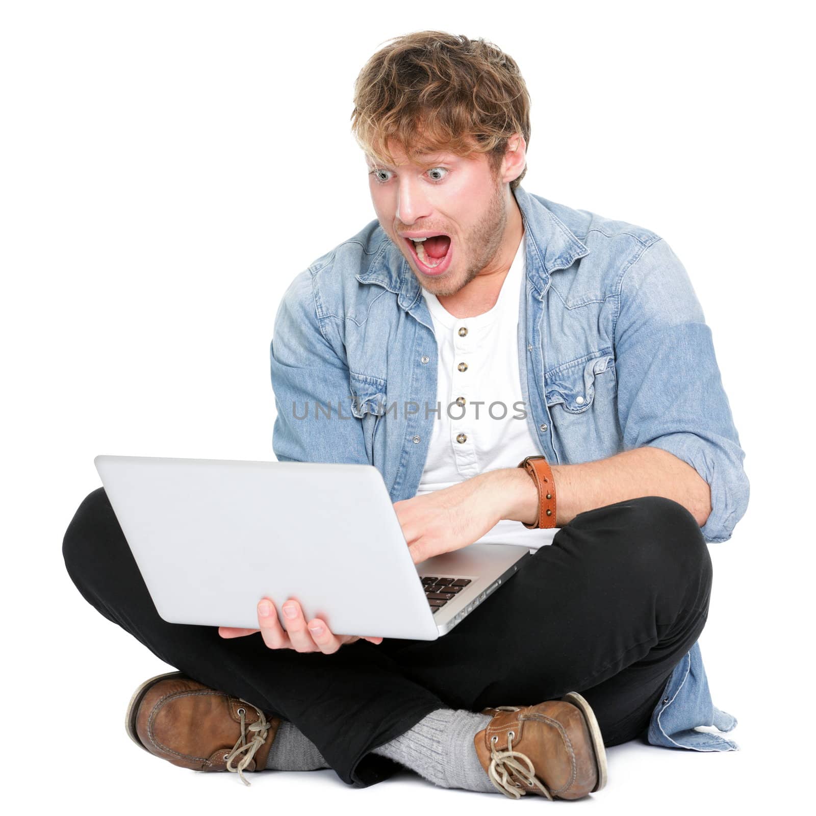 Man surprised with laptop computer looking at screen excited and happy in disbelief. Funny image of young Caucasian male student model sitting on floor isolated on white background.
