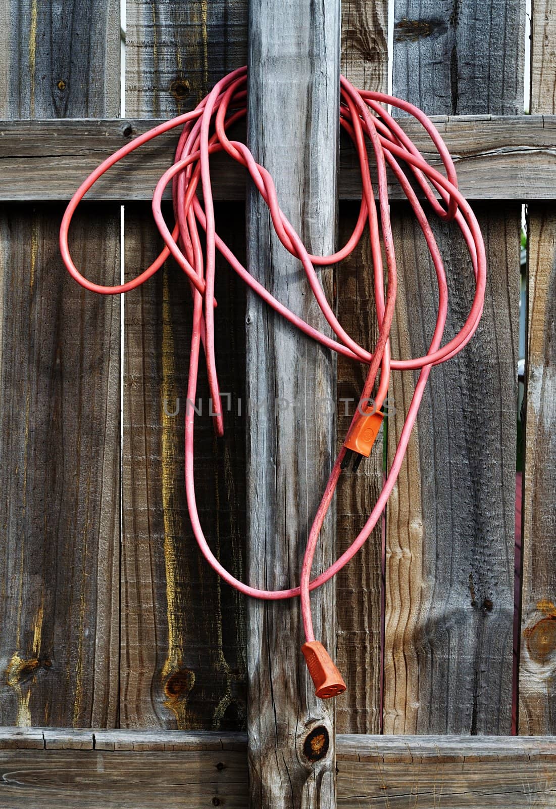 Orange outdoors electric cord wrapped around a wooden fence.