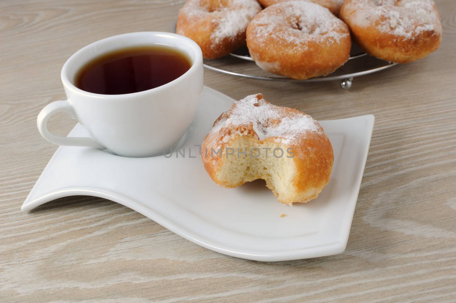 A cup of coffee and donut bitten in the powdered sugar on a plate