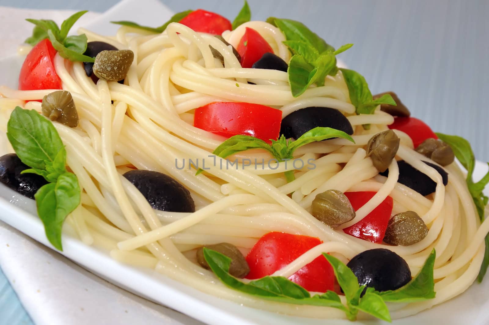 Spaghetti with tomato slices and olives, capers and basil