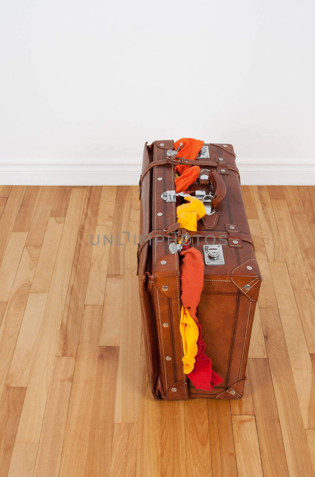 Leather suitcase on a wooden floor, overfilled with clothing.