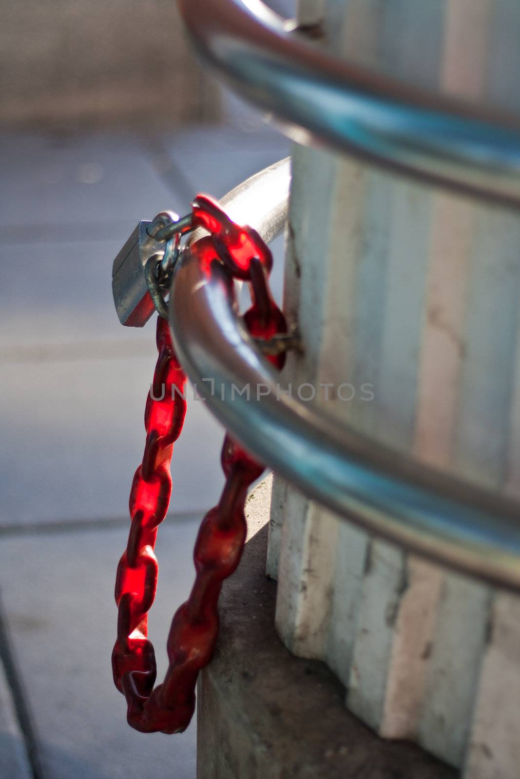 Heavy duty metallic bike lock with red coated chain hangin on it.