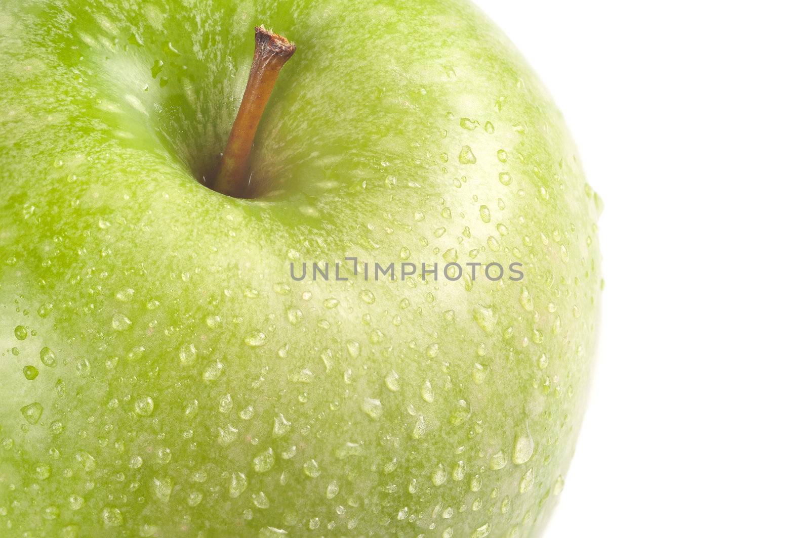 Isolated detail shot of a fresh green apple with stem and drops of water on it.