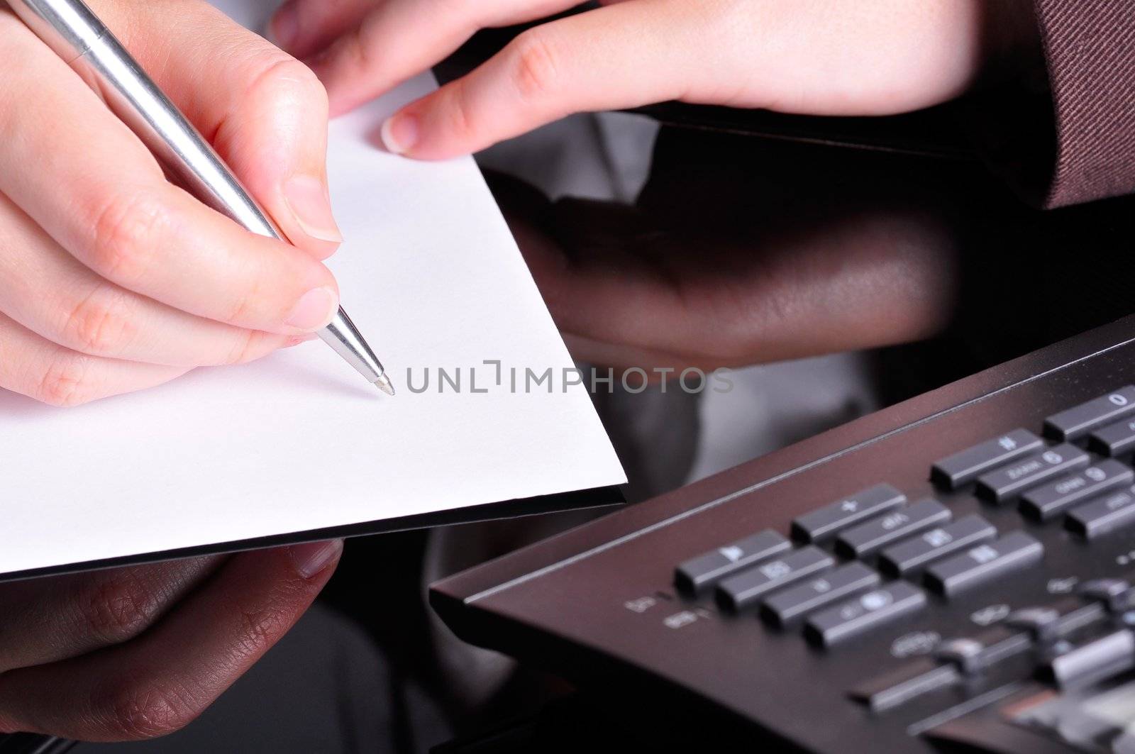 A hand, holding a pen, is ready to write on a document with a telephone next to it.