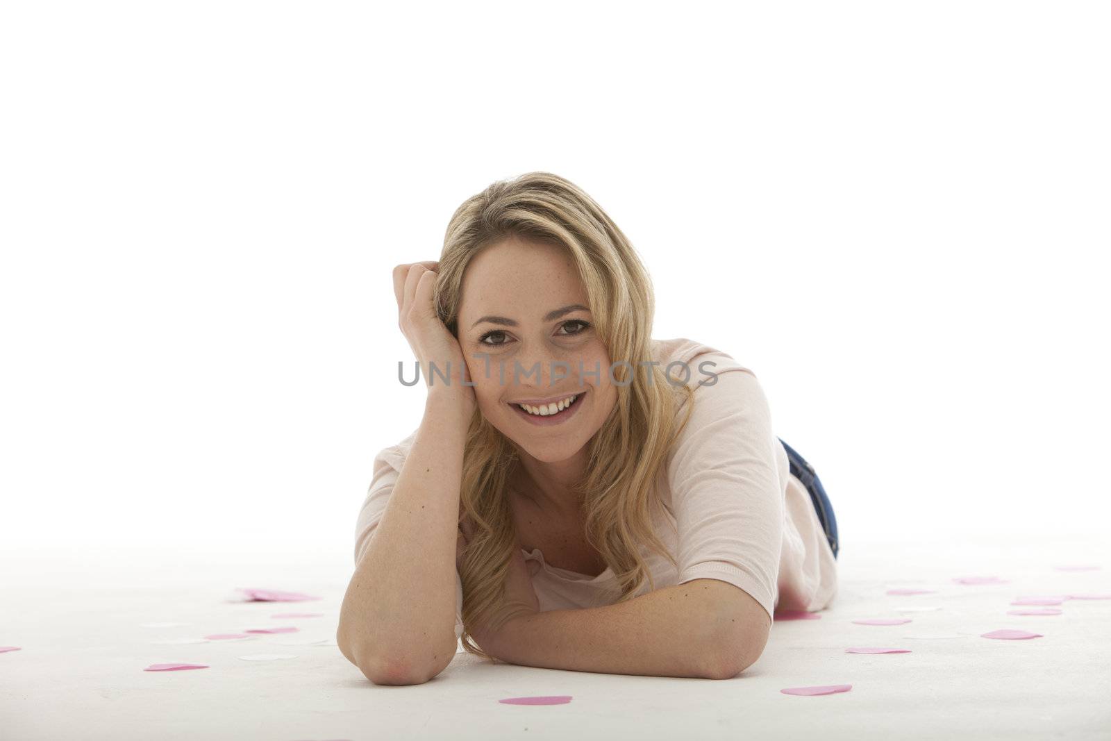 blonde woman wearing a light pink blouse lying on her stomach with her right hand supporting her head on the side and her left hand in front of her on a white background