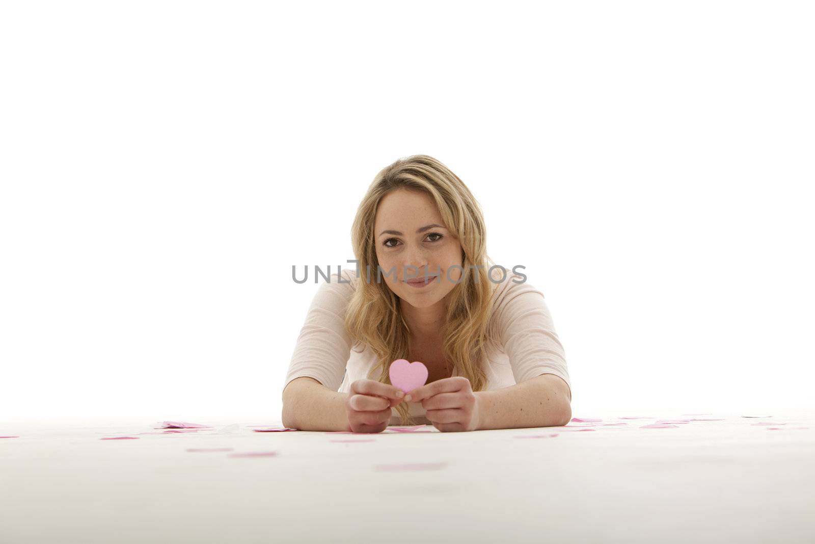 blonde woman on her tummy holding a pink cardboard heart with both hands