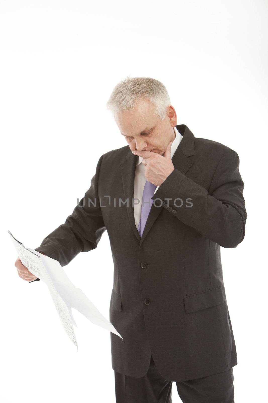 Businessman standing with his hand to his chin checking documents held in his hand
