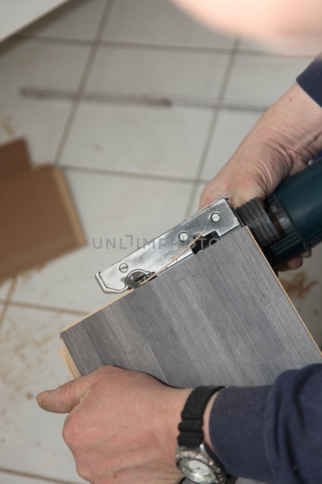 Cropped view of the hands of a handyman trimming tiles with a cutter above a tiled floor in a DIY concept
