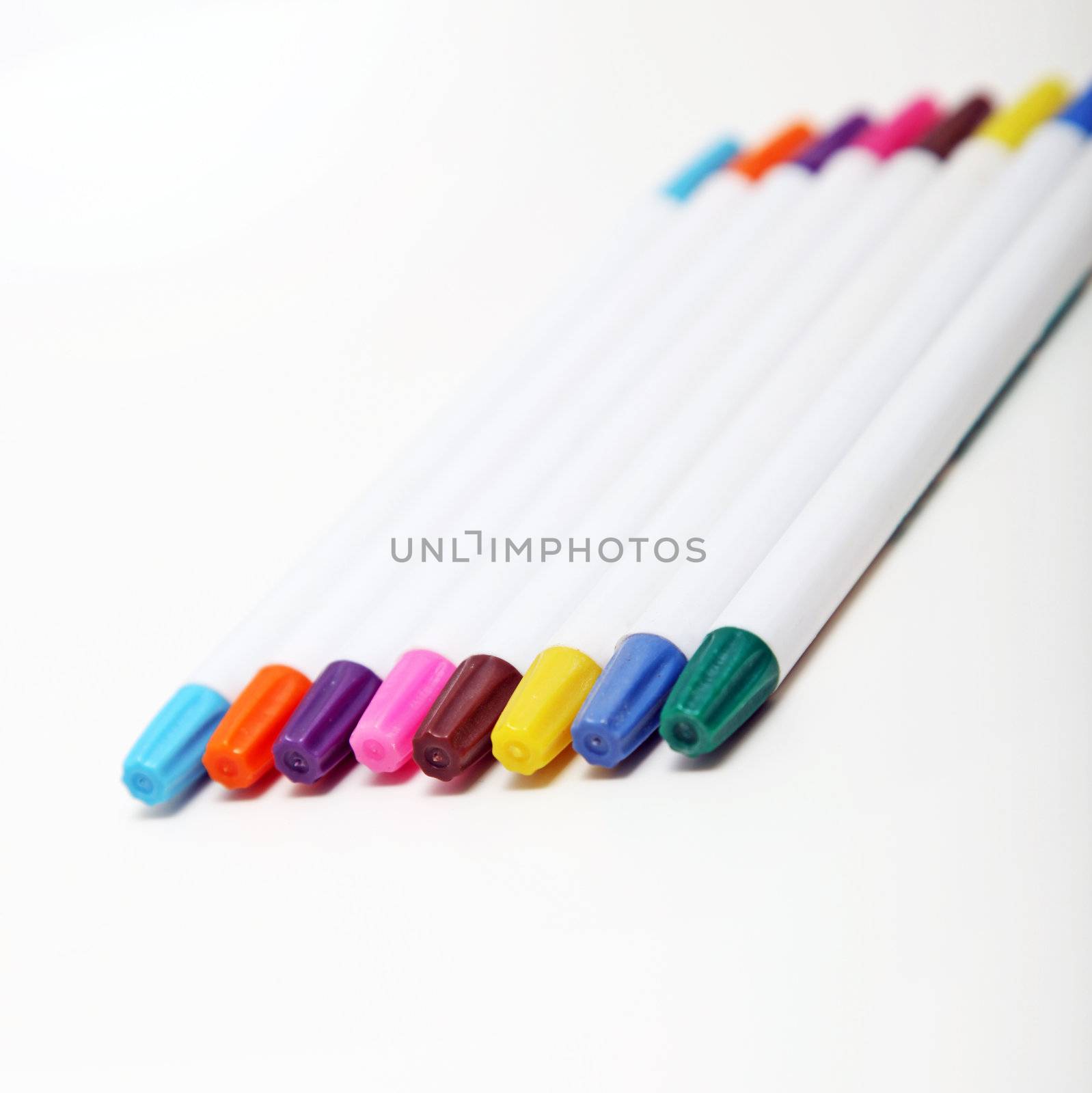 Set of colourful felt tip pens in the colours of the rainbow for use in art lying at an oblique angle on a white background