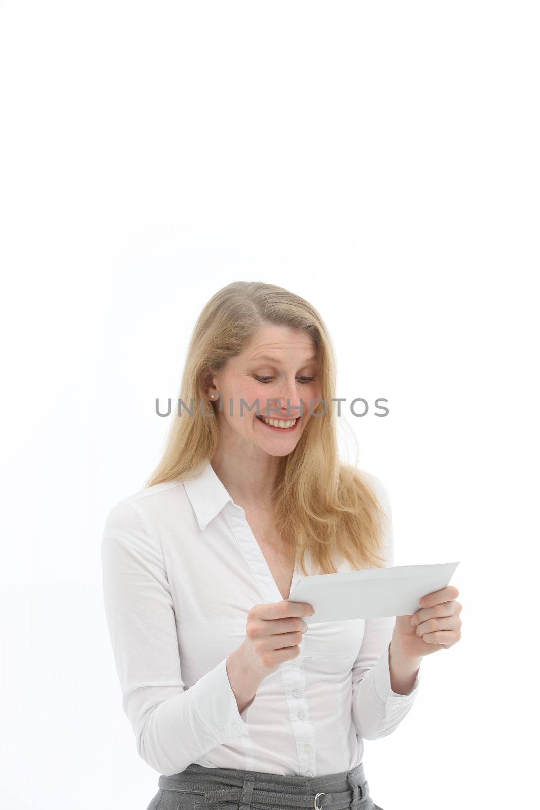 Happy woman with a gleeful grin reading good news in a letter which she is holding in her hands isolated on white