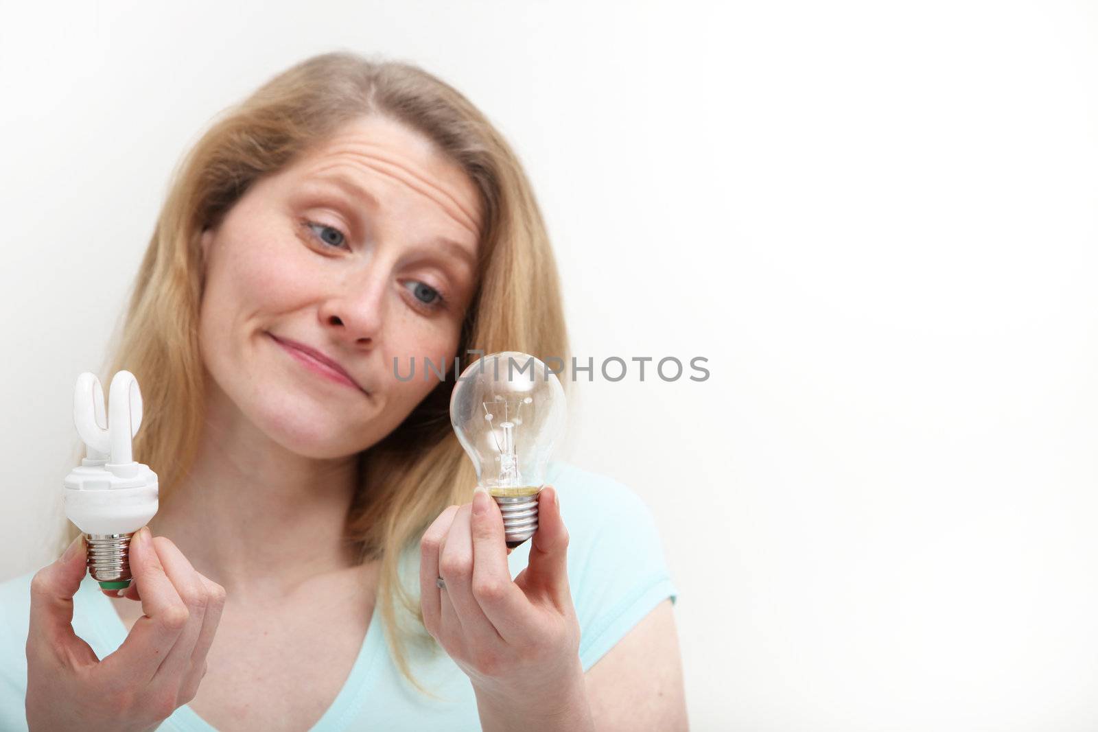 Pretty girl looks disapprovingly at old style lightbulb compared to the new technology type