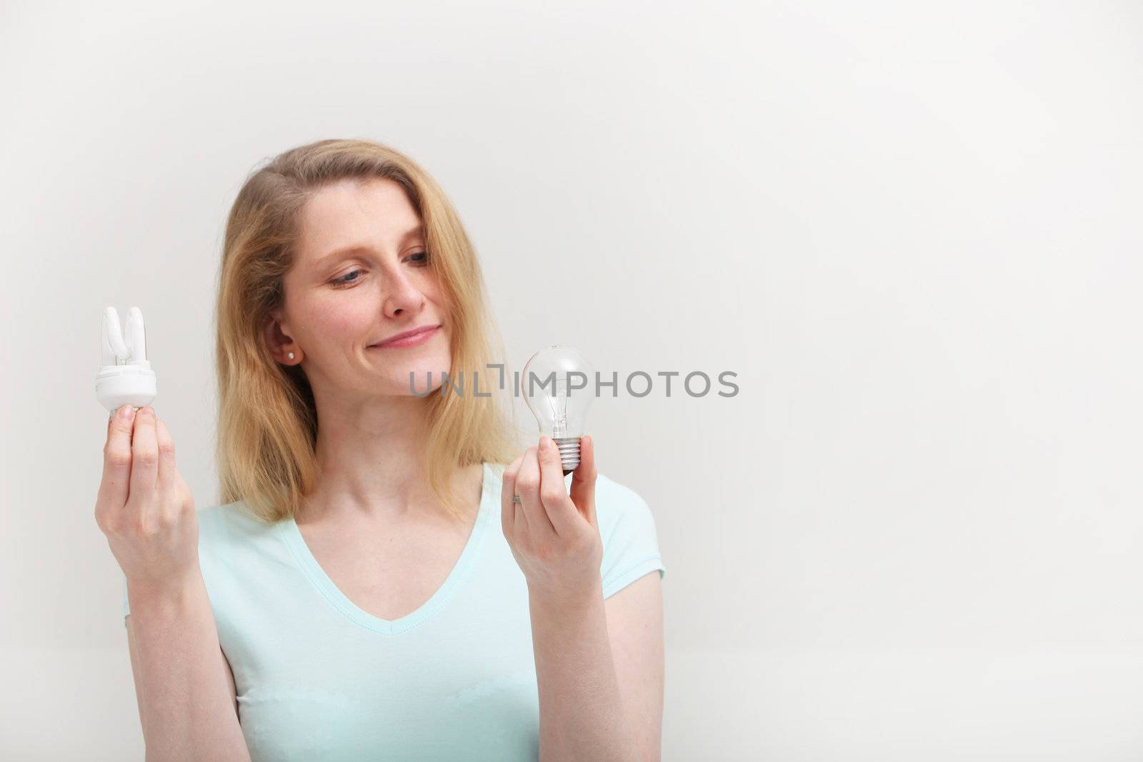 Woman holding an eco-friendly spiral fluorescent bulb in one hand looks at an old inefficient incandescent bulb in her other hand with regret as she makes her choice