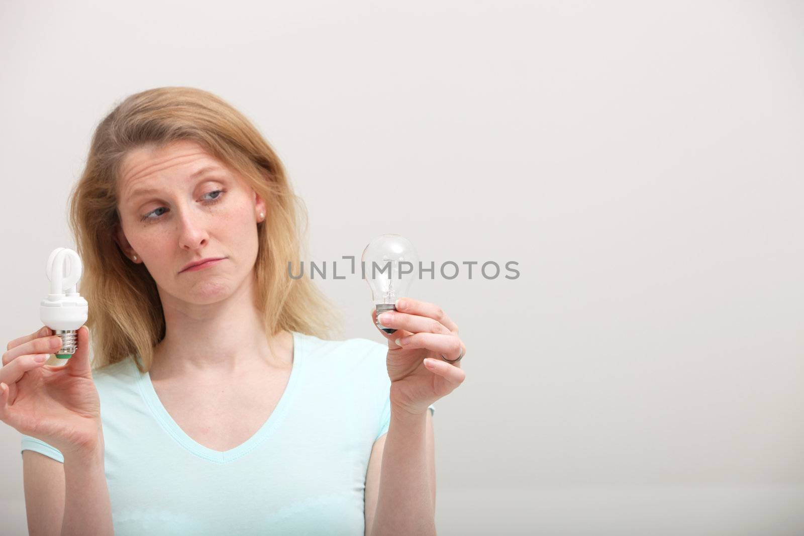 Woman holding an eco-friendly spiral light bulb in one hand is eyeing an old incandescent bulb in her other hand with disdain