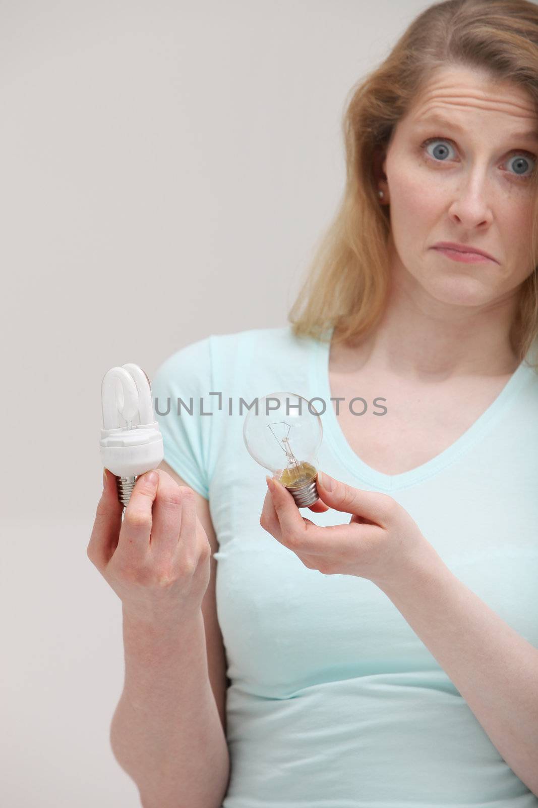 Woman holding a new efficient eco-bulb and an inefficient costly incandescent bulb with a look of complete ignorance