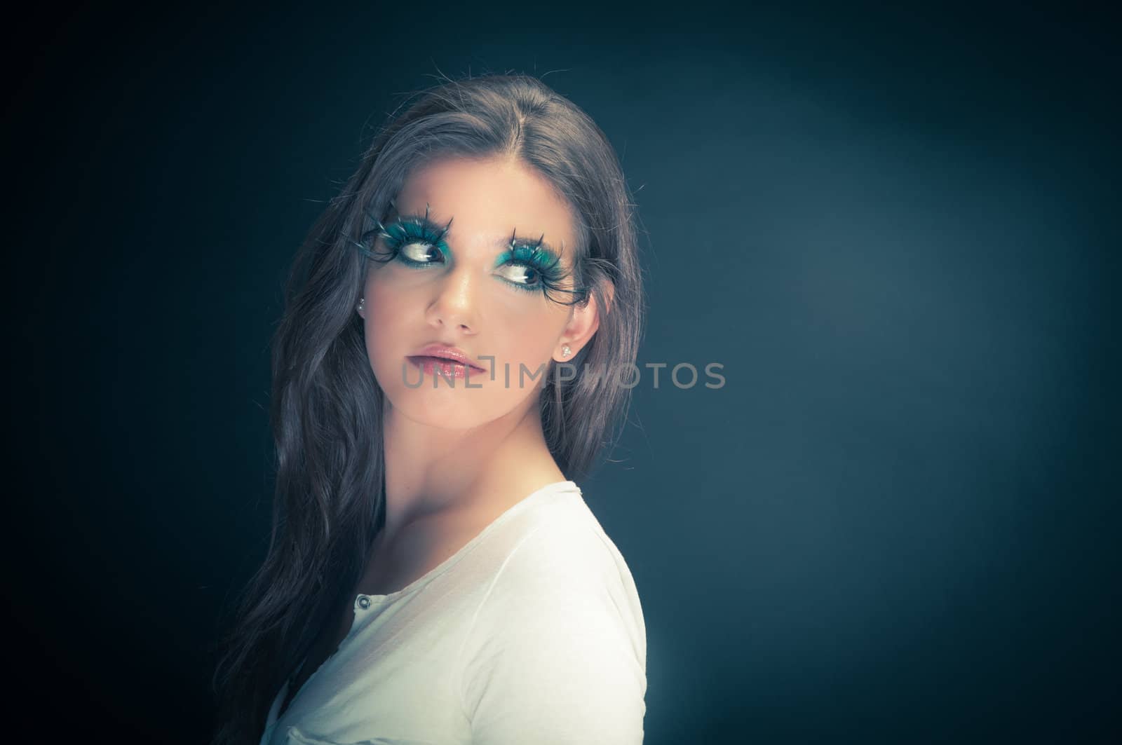 Young woman in the studio with extreme makeup against dark background