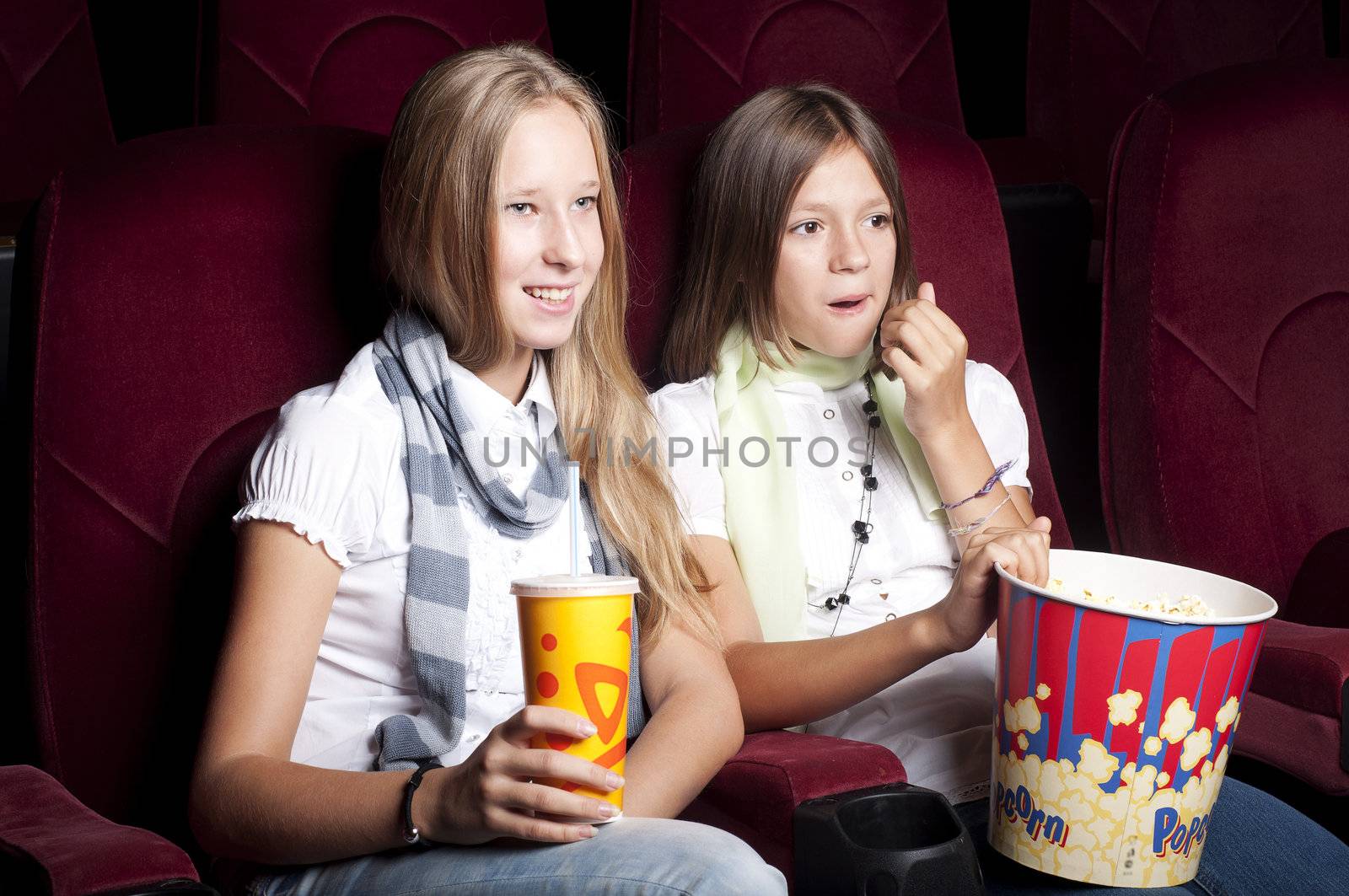 two girls look three-dimensional cinema, sitting in the glasses, eat popcorn, drink drink