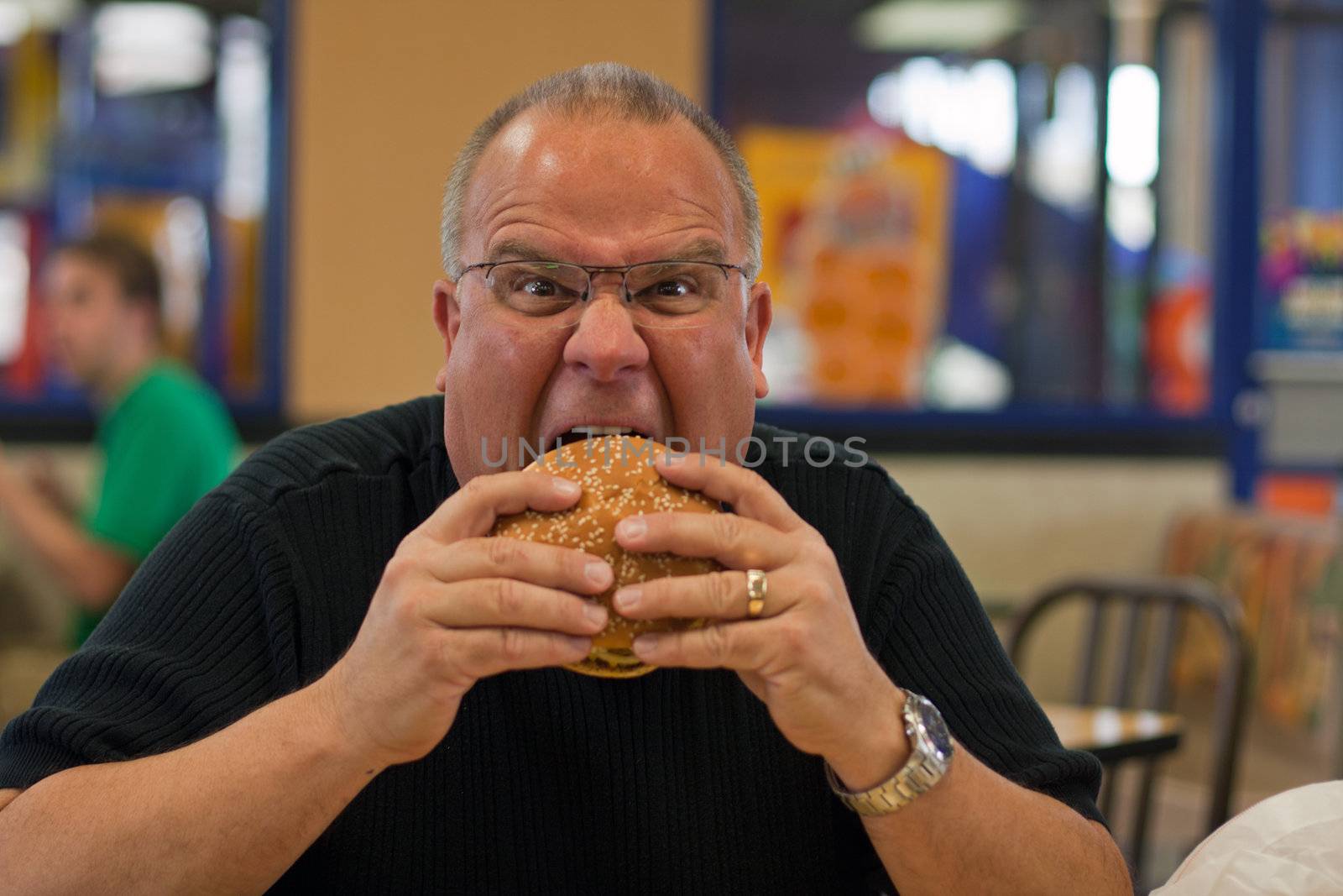man eating burger in fast food restaurant by GunterNezhoda