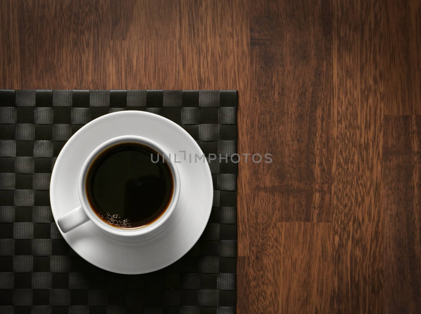 Steaming hot cup of black coffee on wooden table and dark tablemat