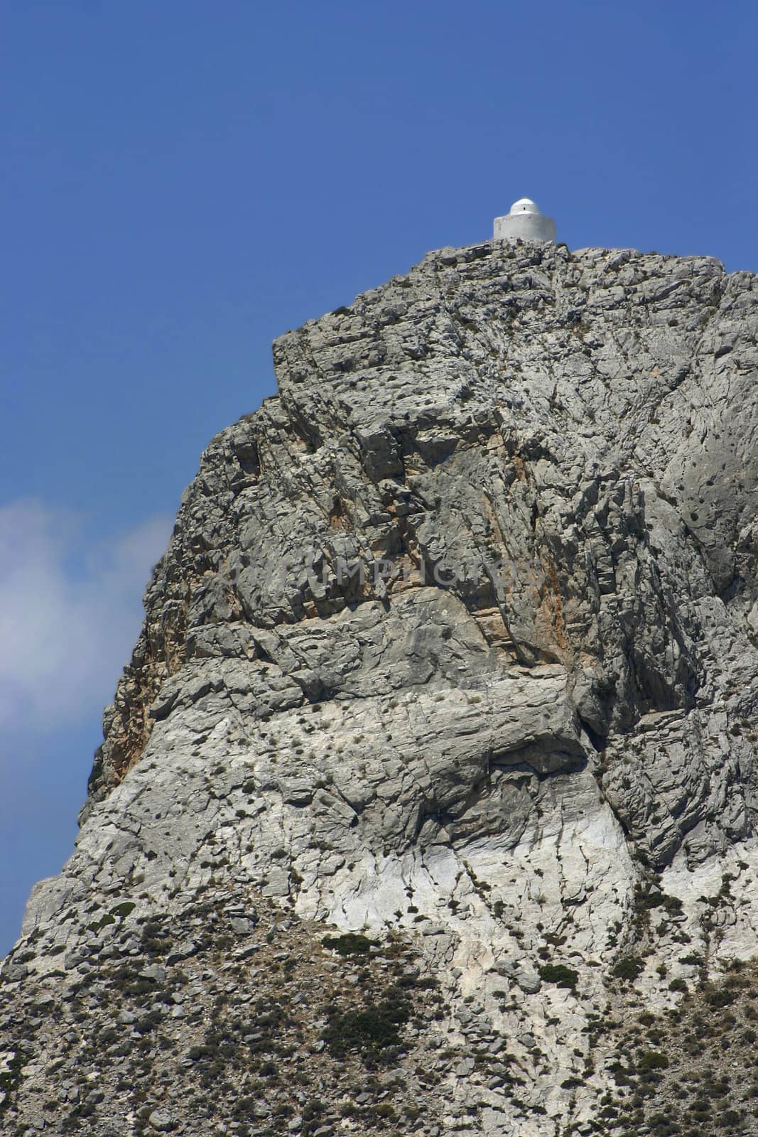 White Greek church high on steep mountain cliff peak