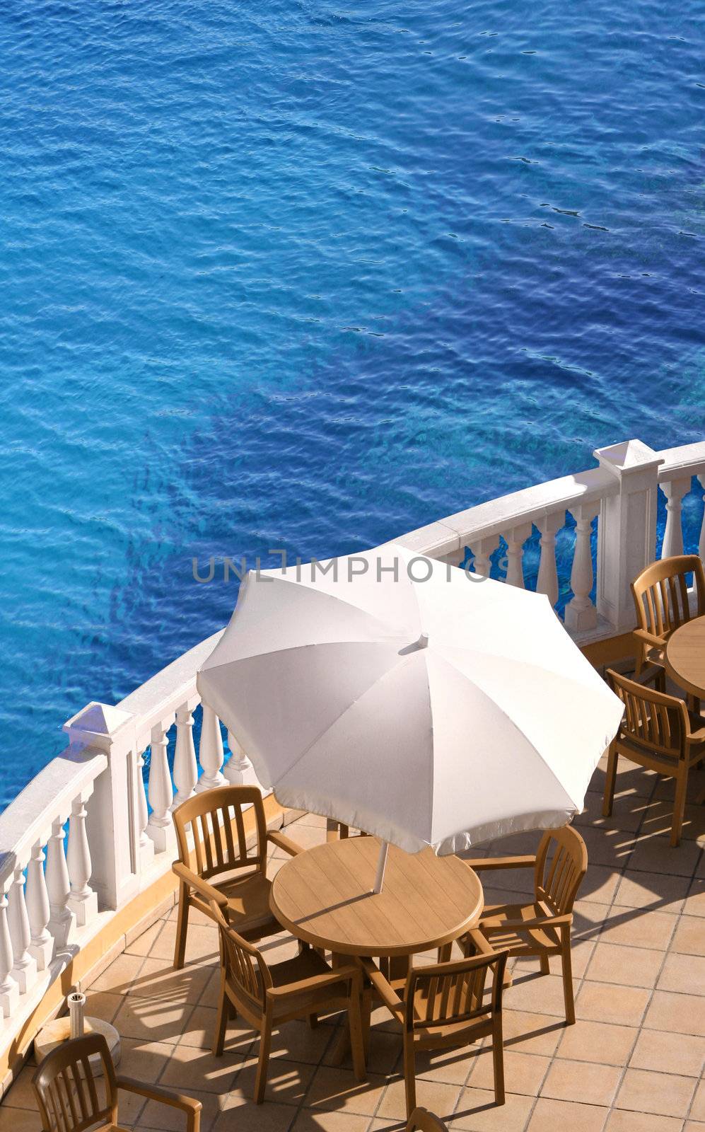 Holiday terrace chairs and table with sun umbrella beside a turquoise blue water