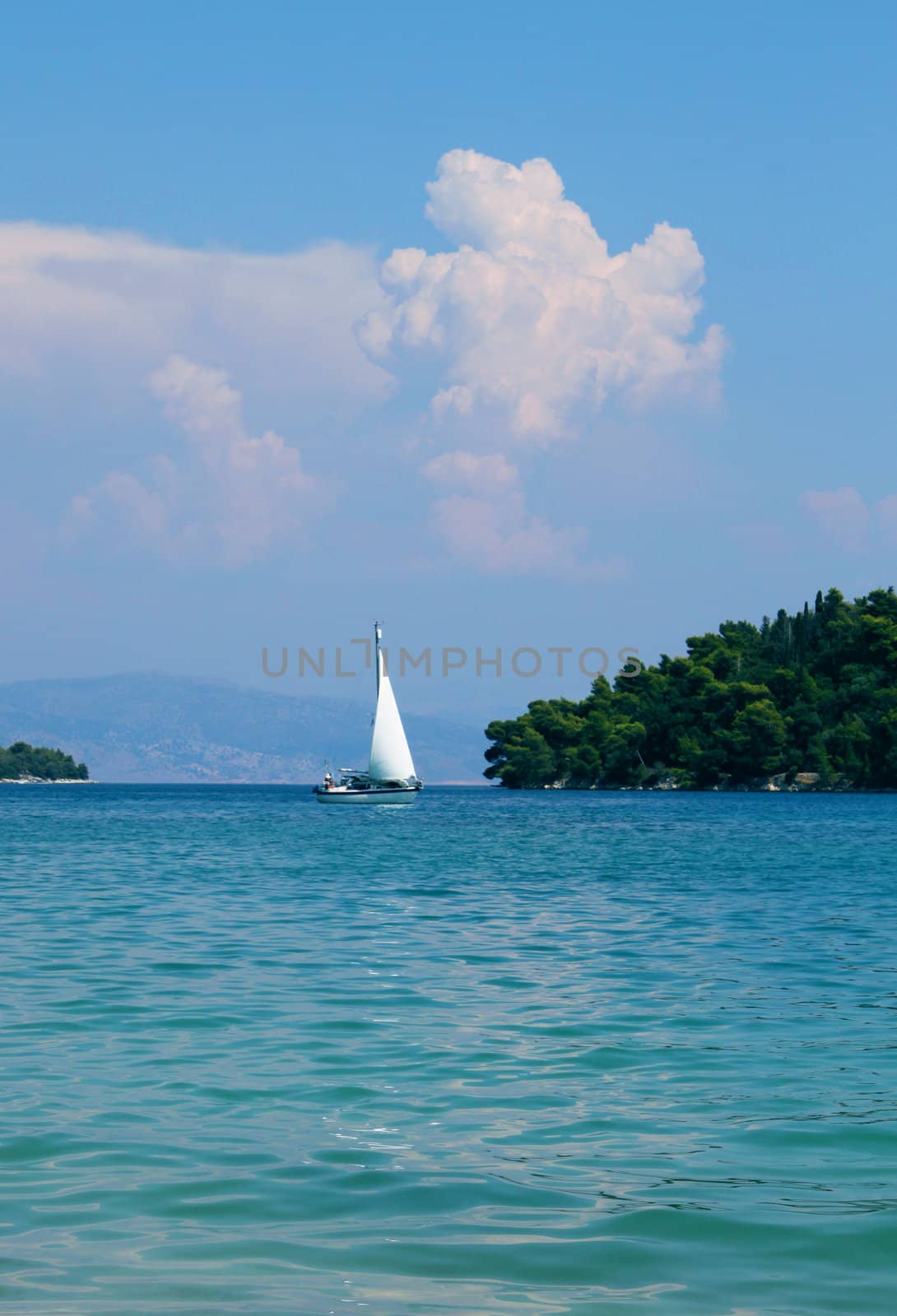 Lone sailboat approaching peaceful paradise island on turquoise sea