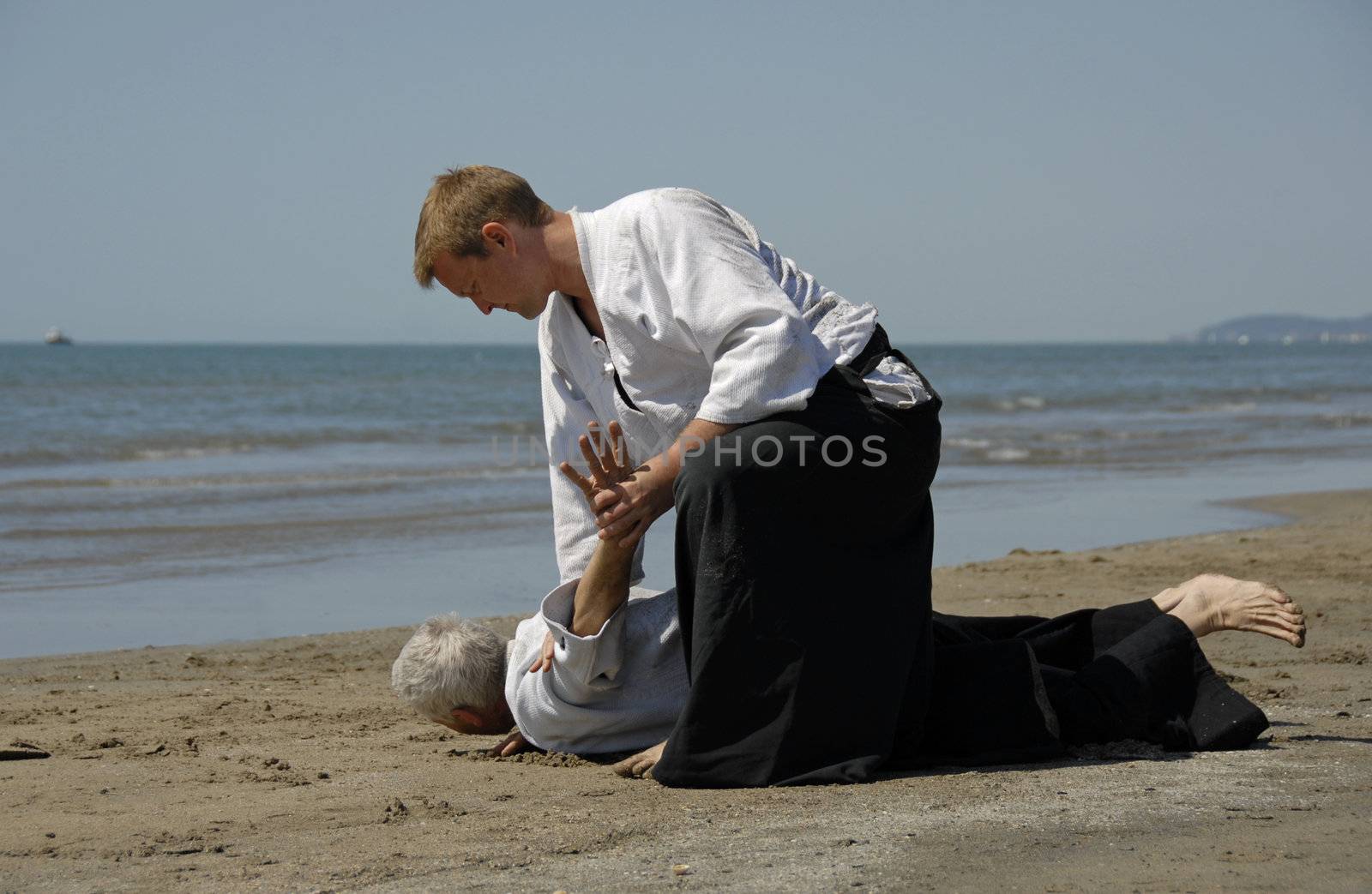 Two adults are training in Aikido on the beach