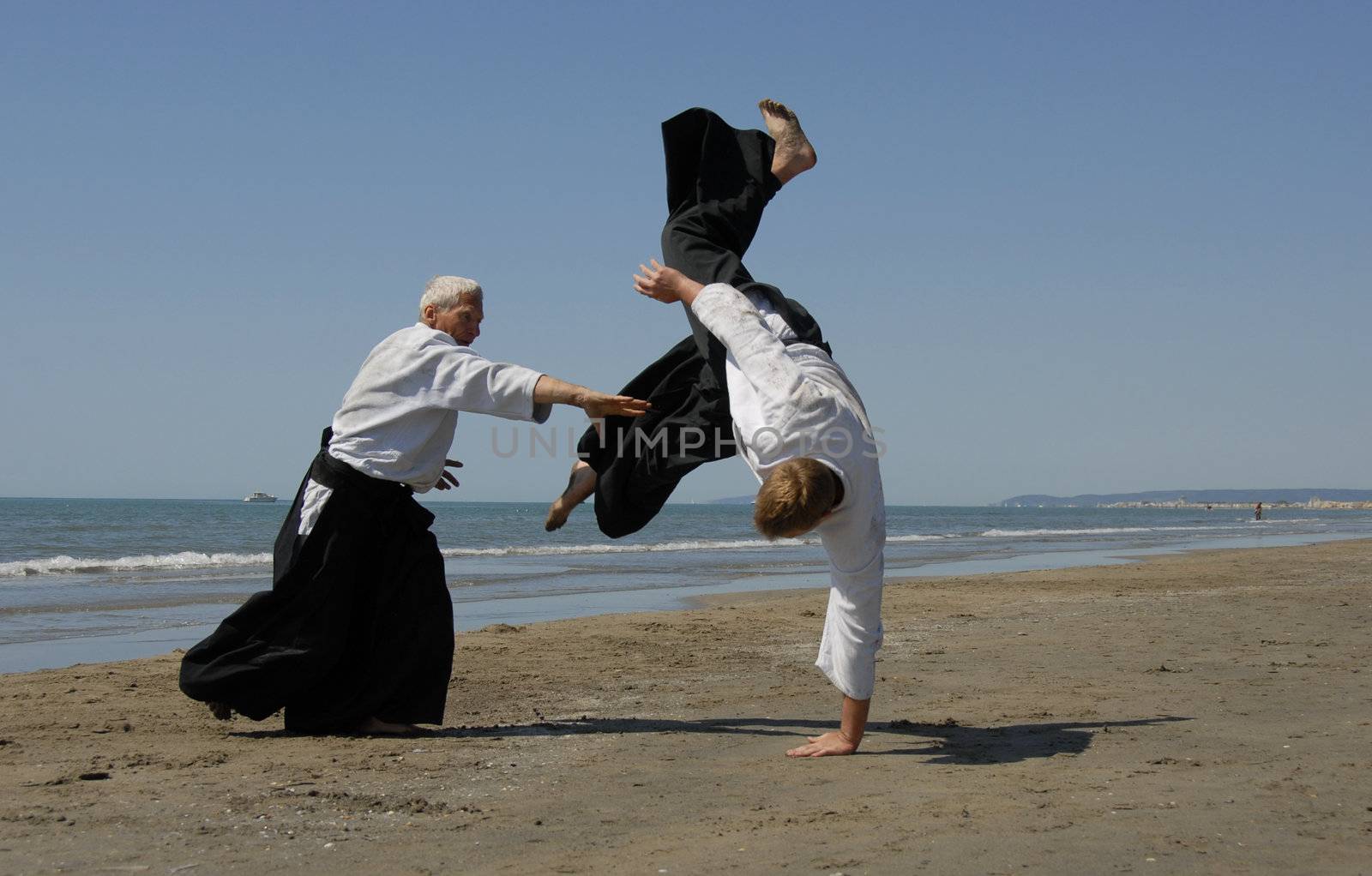 Two adults are training in Aikido on the beach