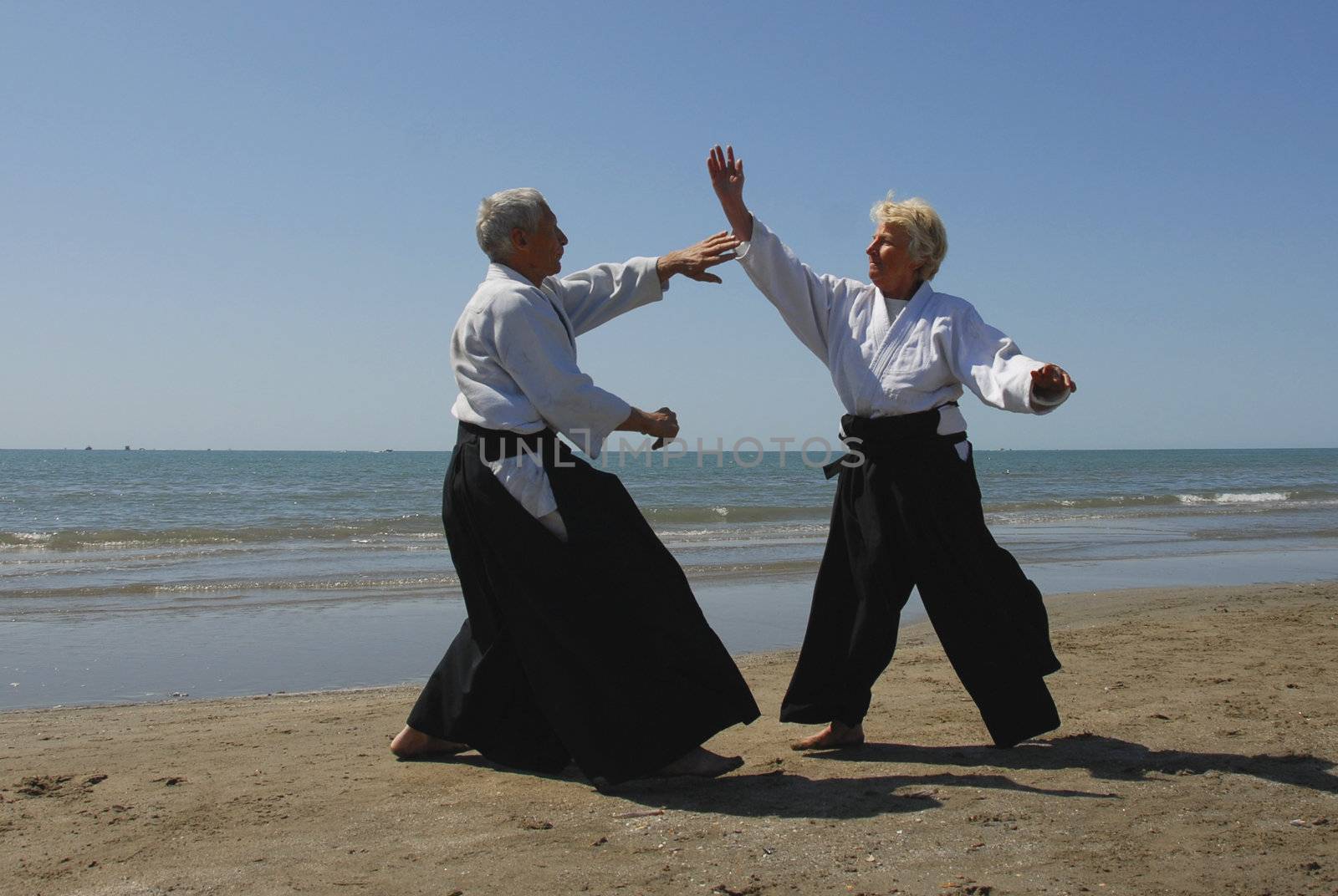 Two adults seniors are training in Aikido on the beach