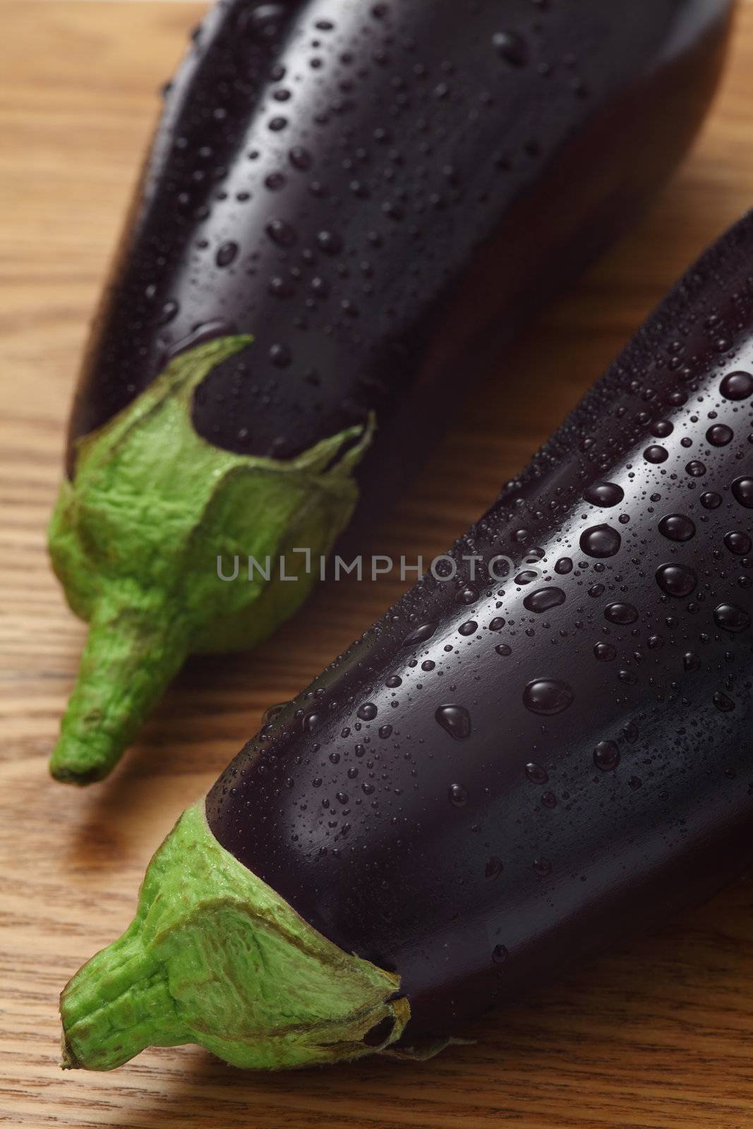Photo of two eggplants with water droplets on a wood table.