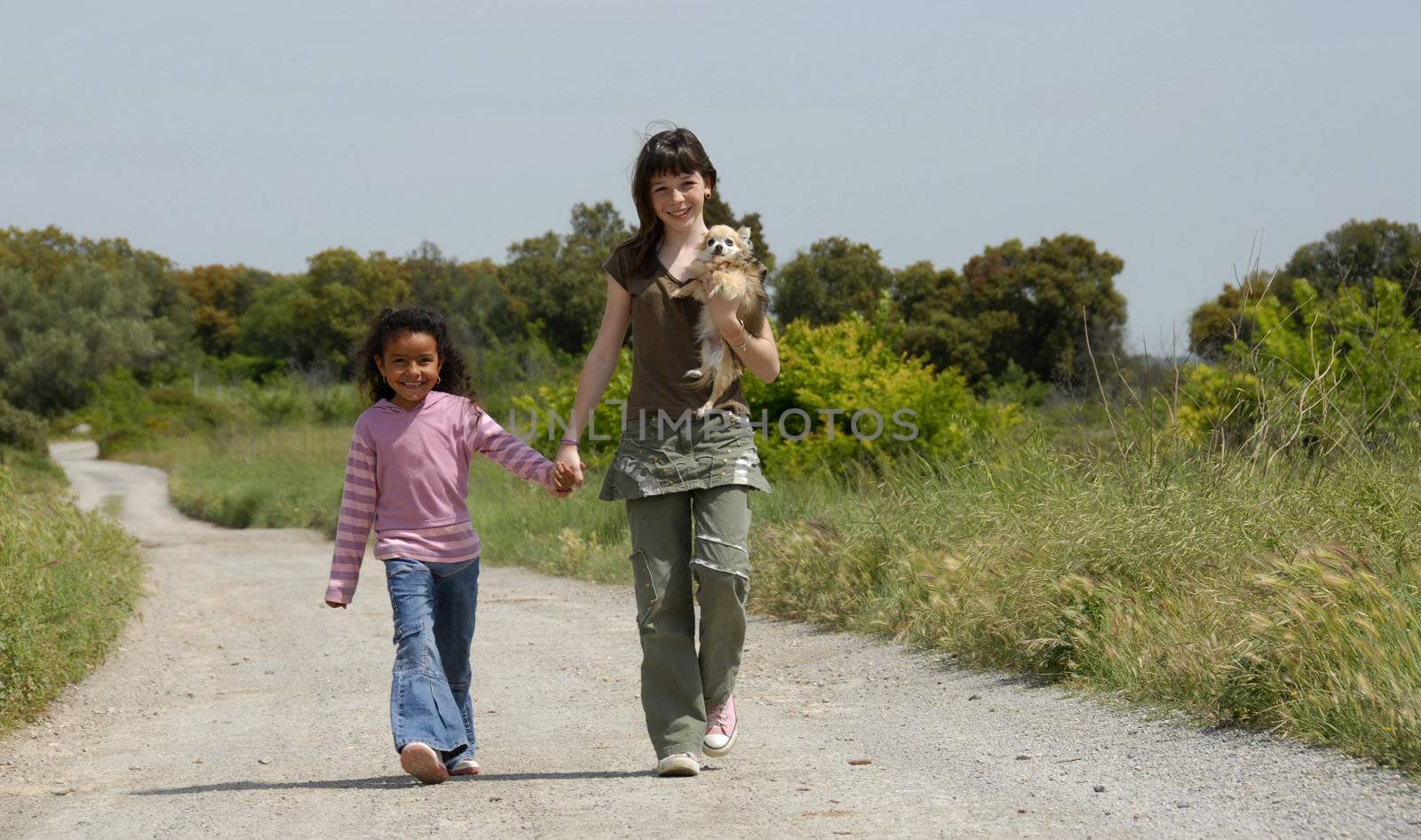 two sisters walking in a little road in the nature with their chihuahua