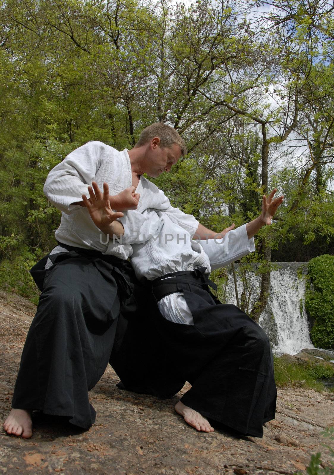 Two adults are training in Aikido in front of a waterfall