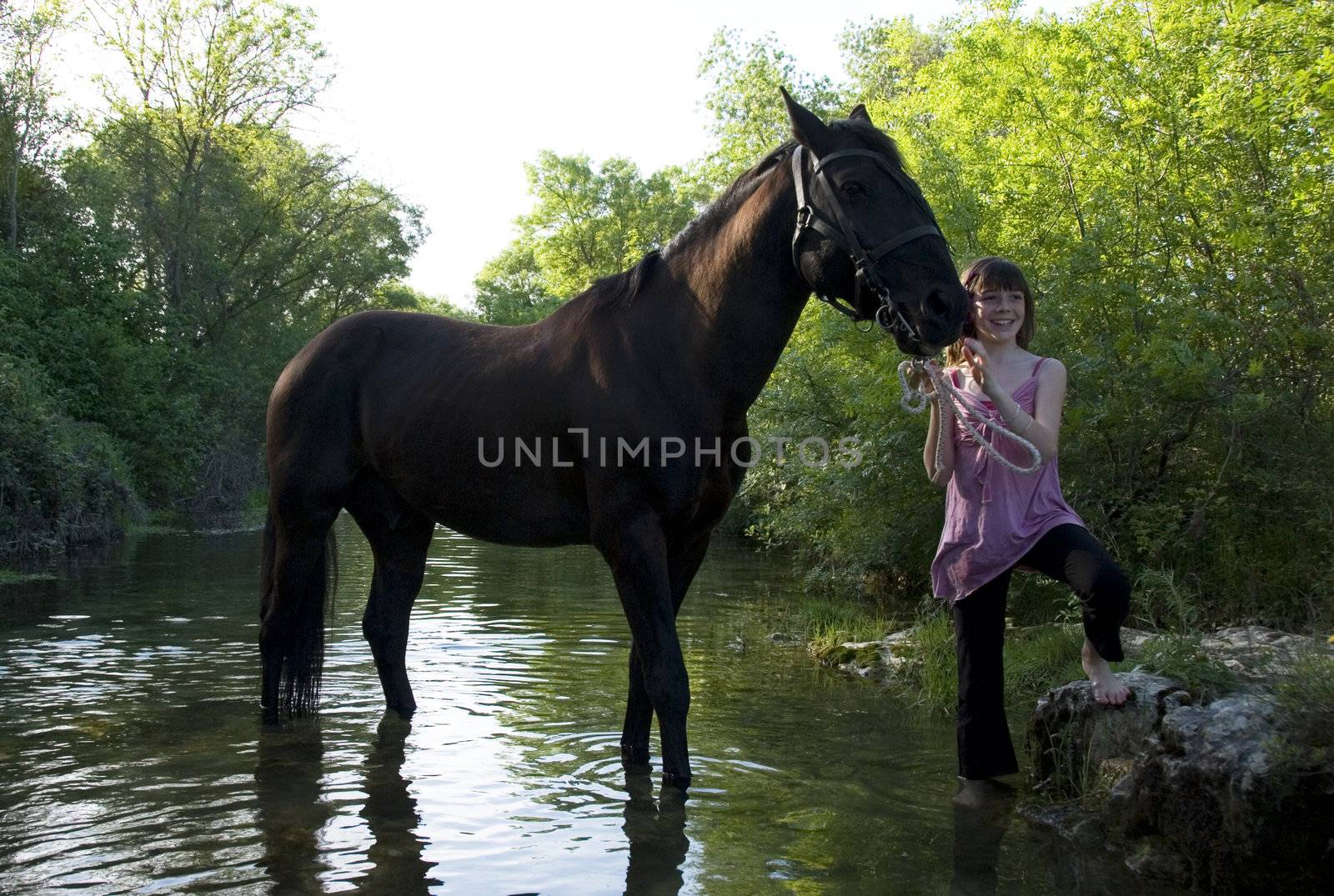 young teenager and her black horse in a river