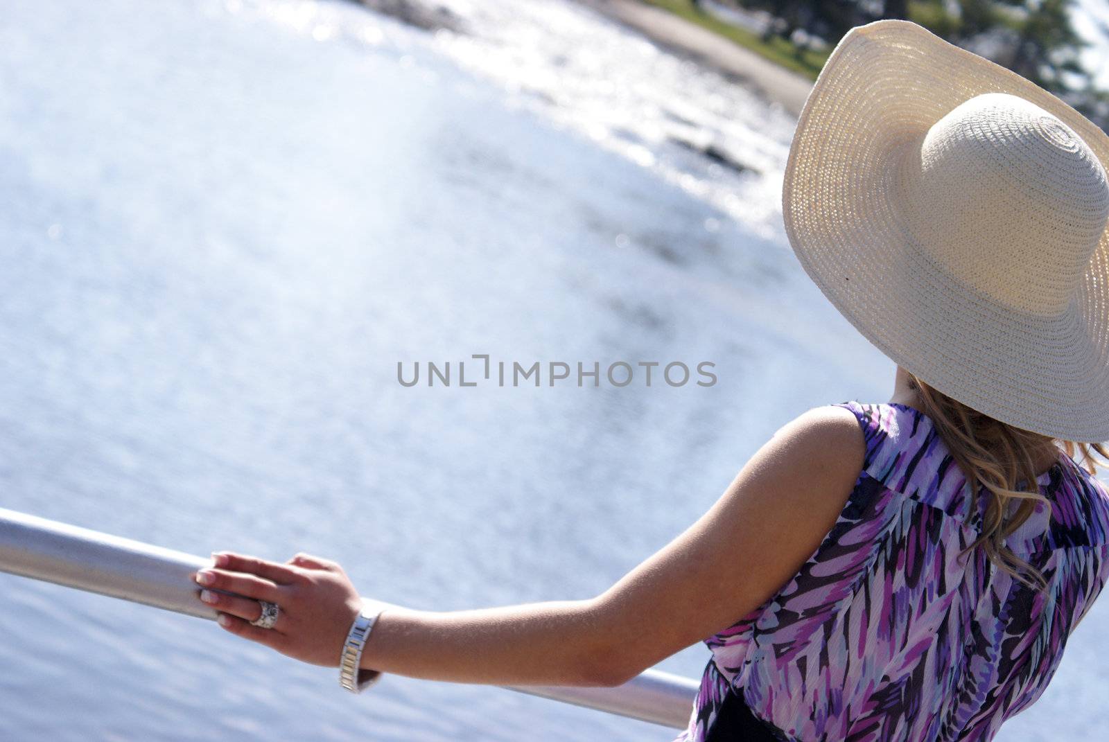 A young woman stands at the railing by the riverside on this sunny day.