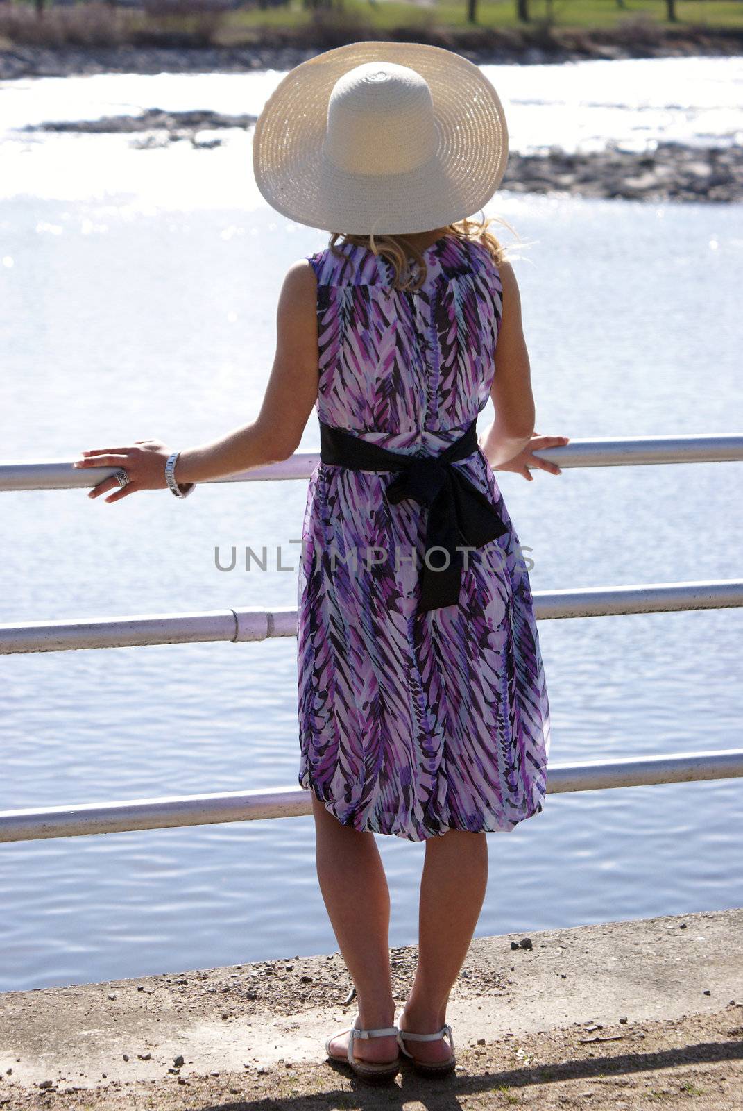A young woman stands at the railing by the riverside on this sunny day.