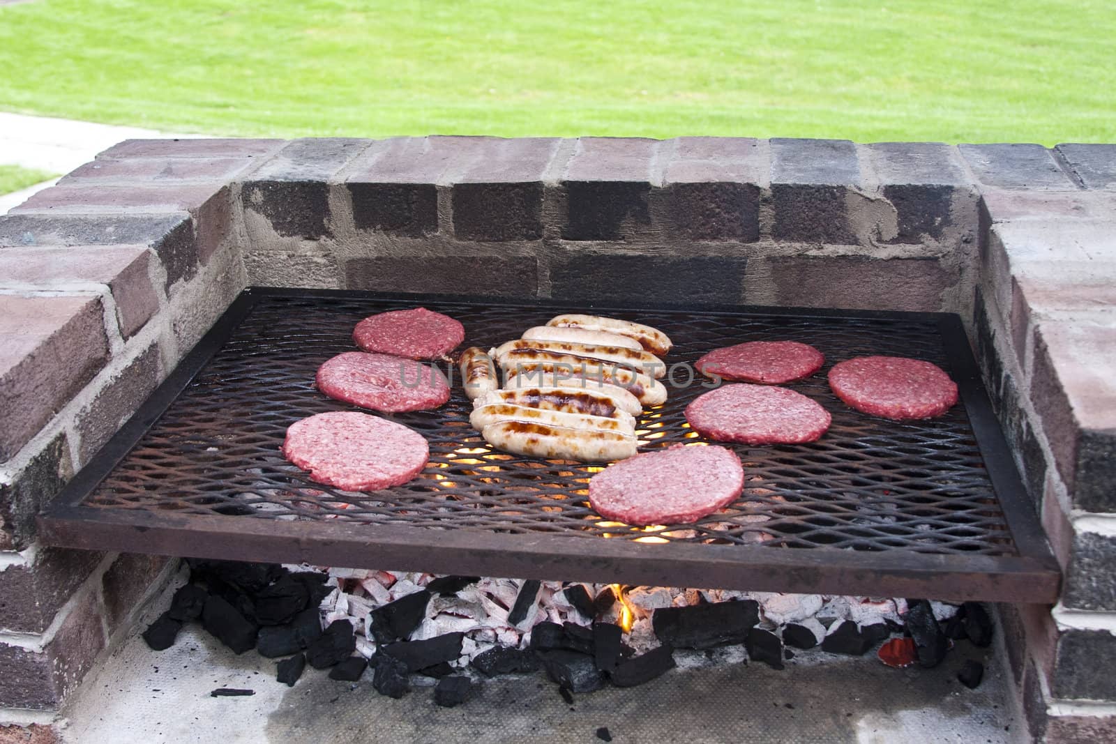 Burgers and sausages cooking on a brick barbeque