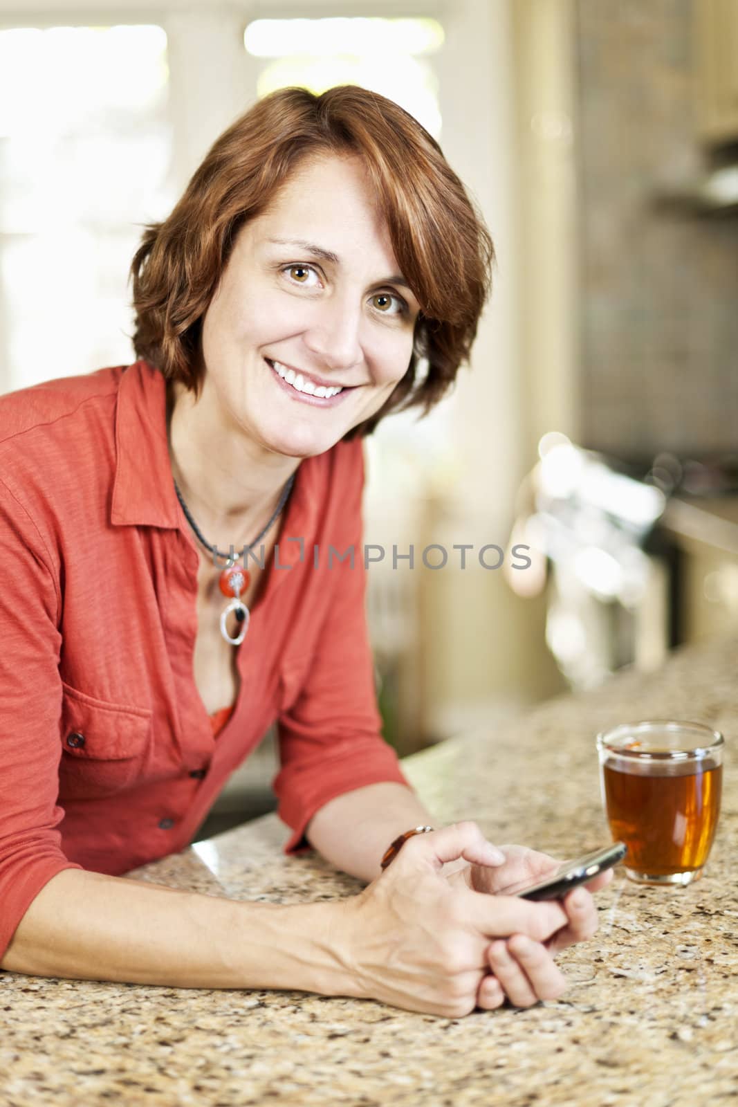 Smiling mature woman texting on phone in kitchen at home