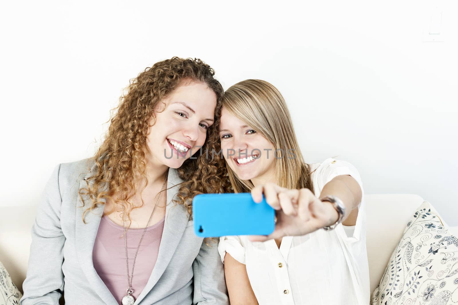 Two smiling women using cellular mobile phone to take a picture