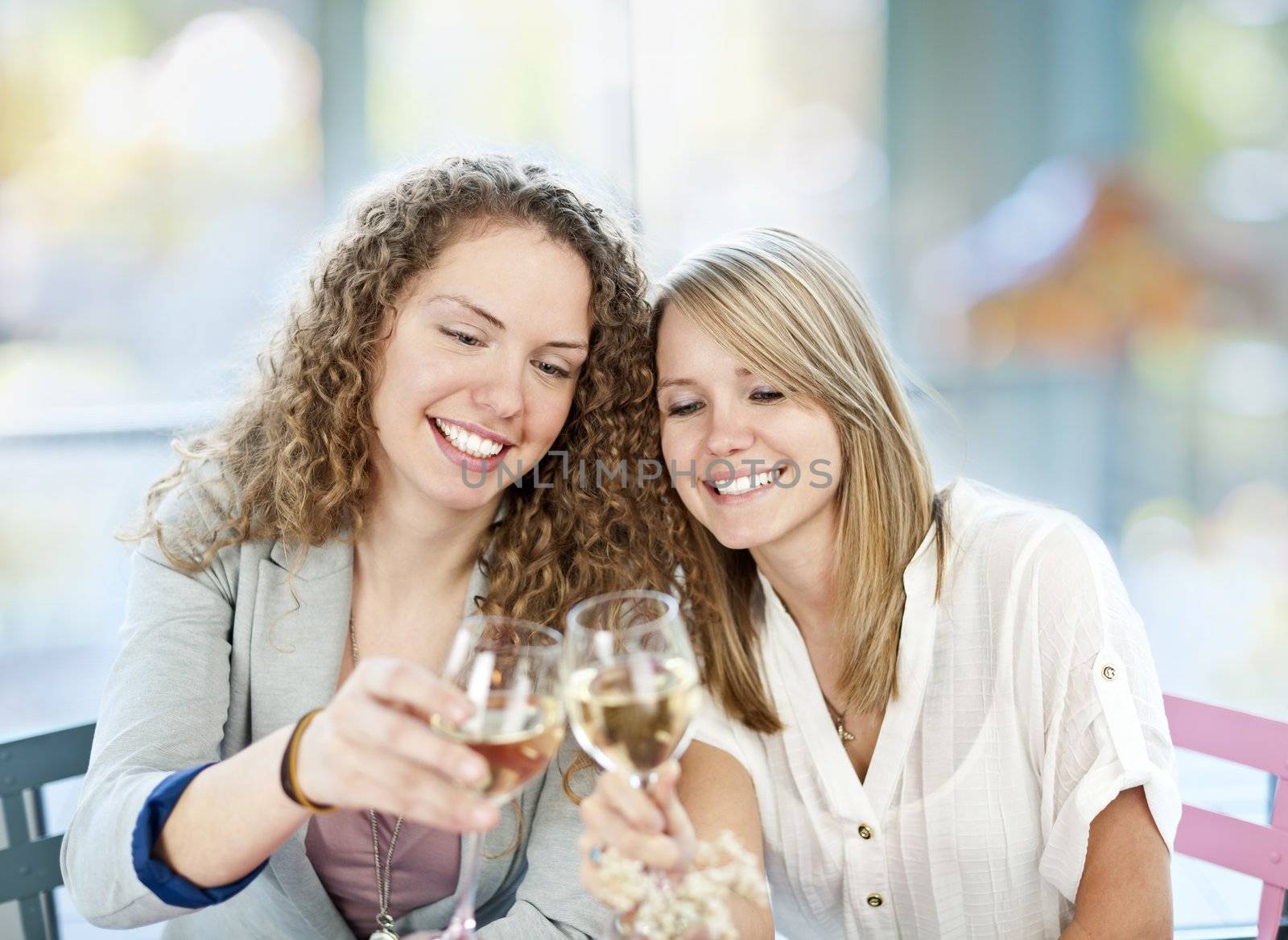 Two happy women in cafe celebrating with glasses of white wine
