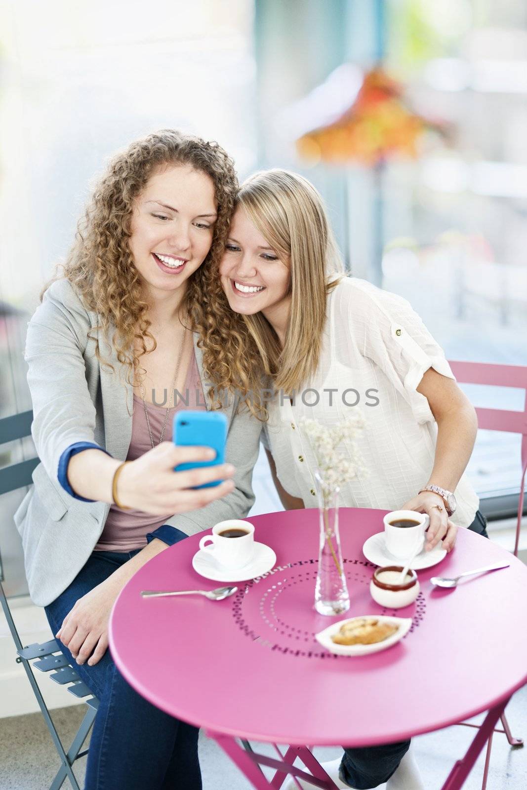 Two smiling women looking at smart phone in cafe