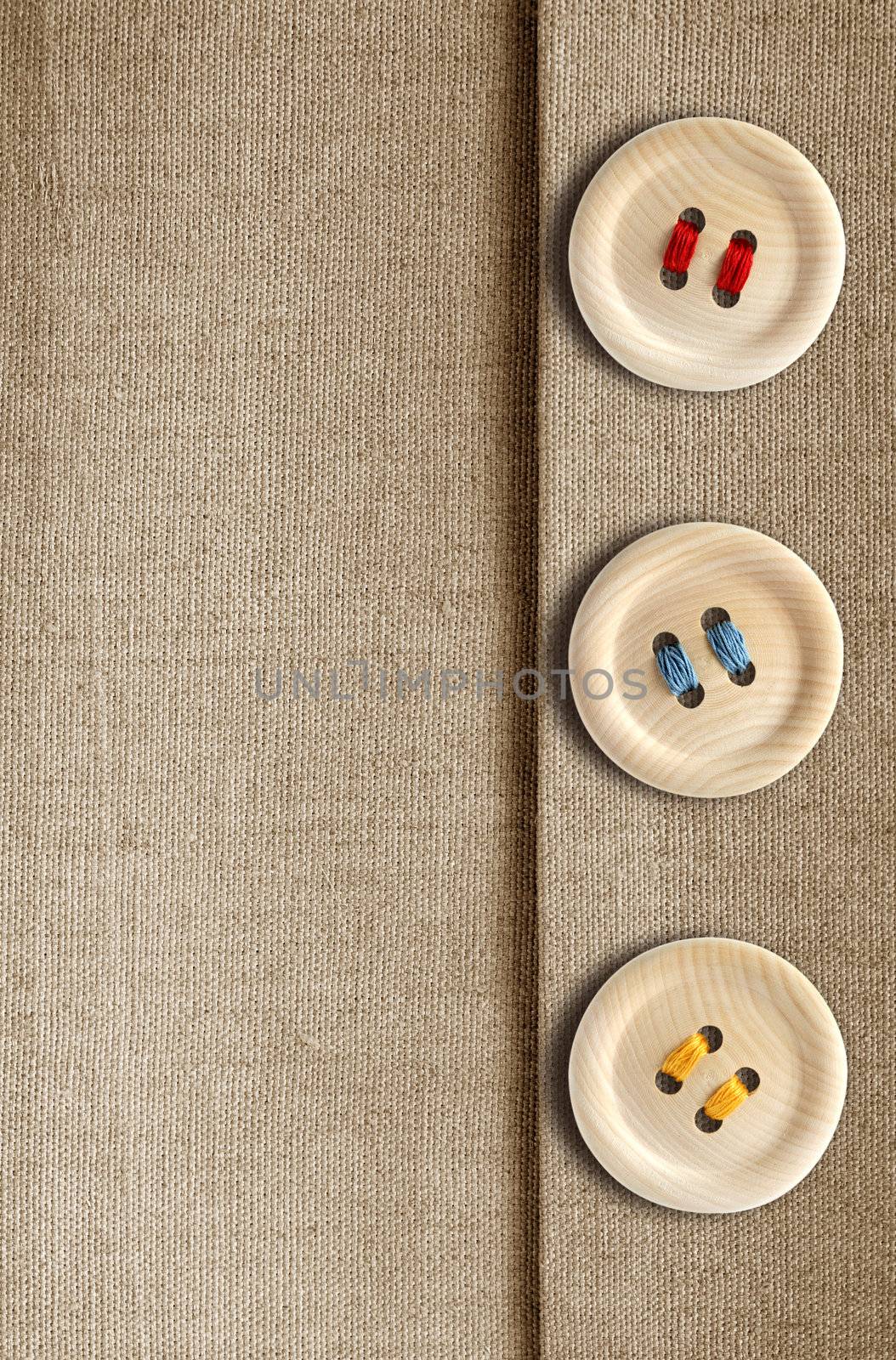 Three wooden button with colored threads on canvas background