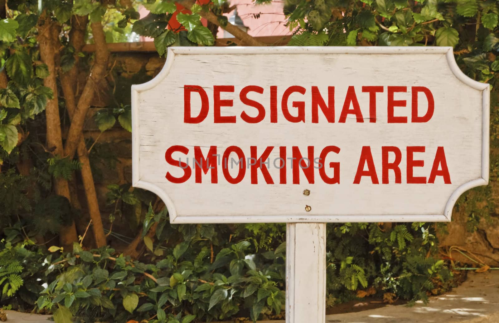 Free standing designated smoking area sign in the corner of a garden area