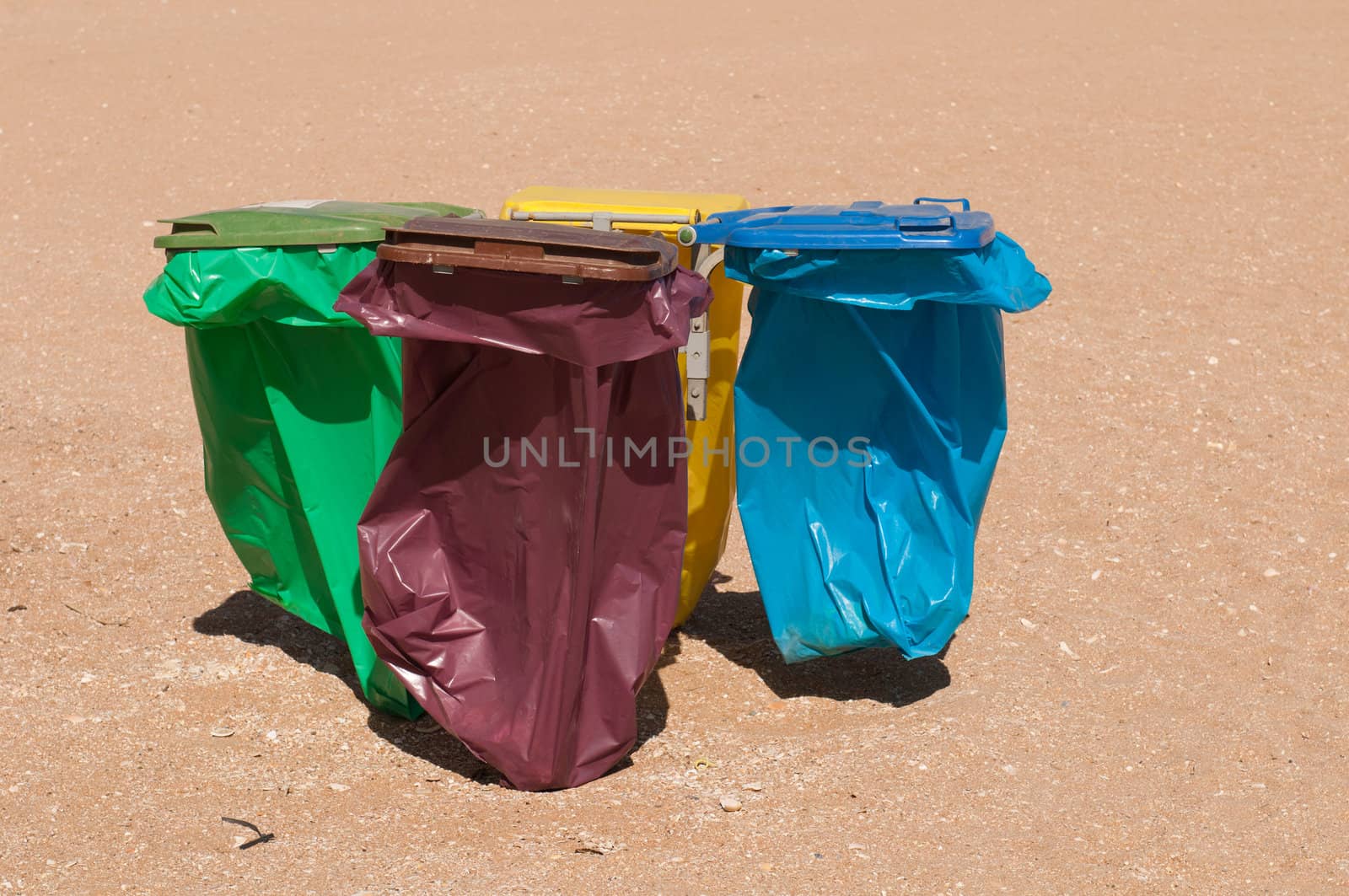 four colorful recycle bins on a beach